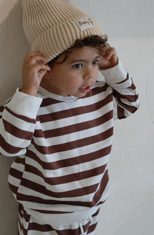 A young toddler wearing the Camden chocolate brown striped pullover and a cream Bobby G beanie.
