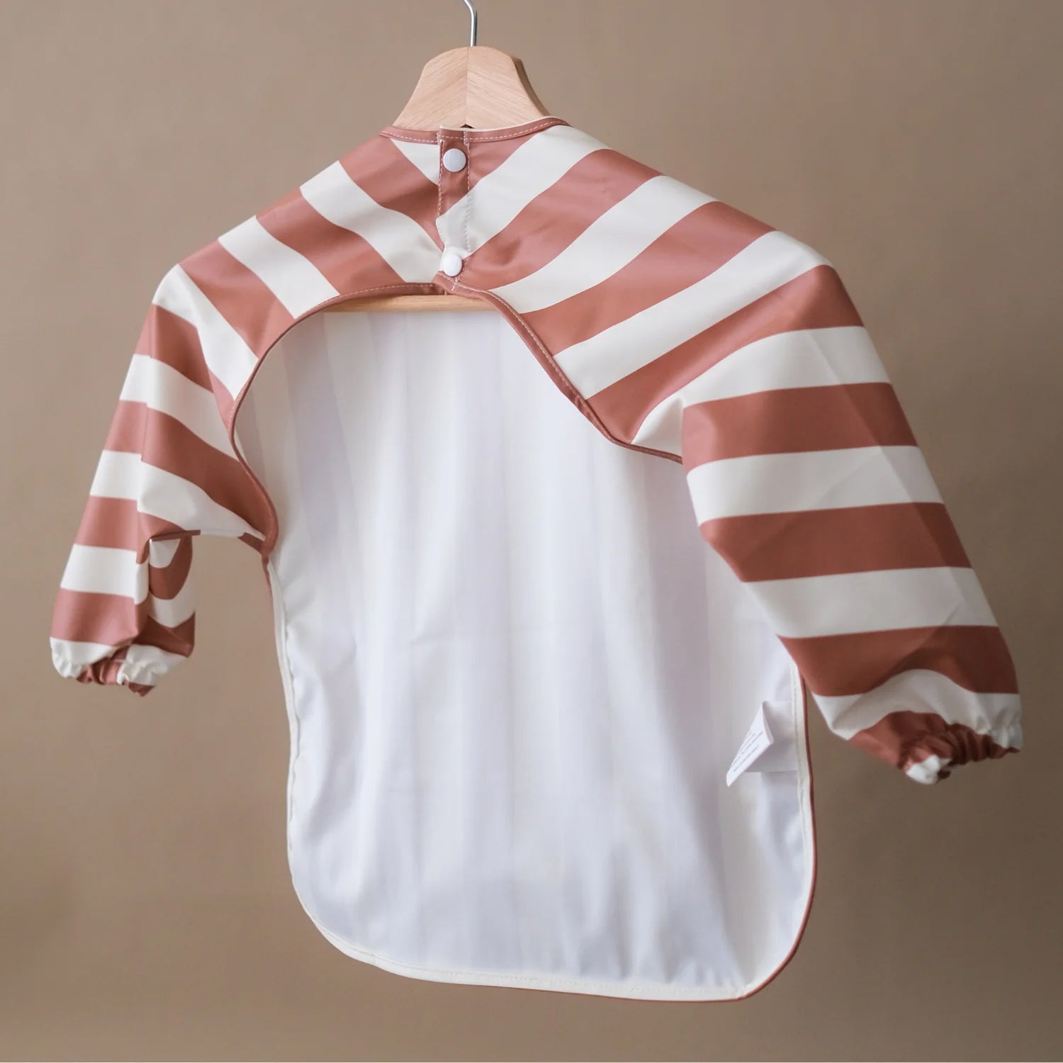 ROMMER Smock Bib in Cinnamon Stripe hanging on a coat hanger from the back.