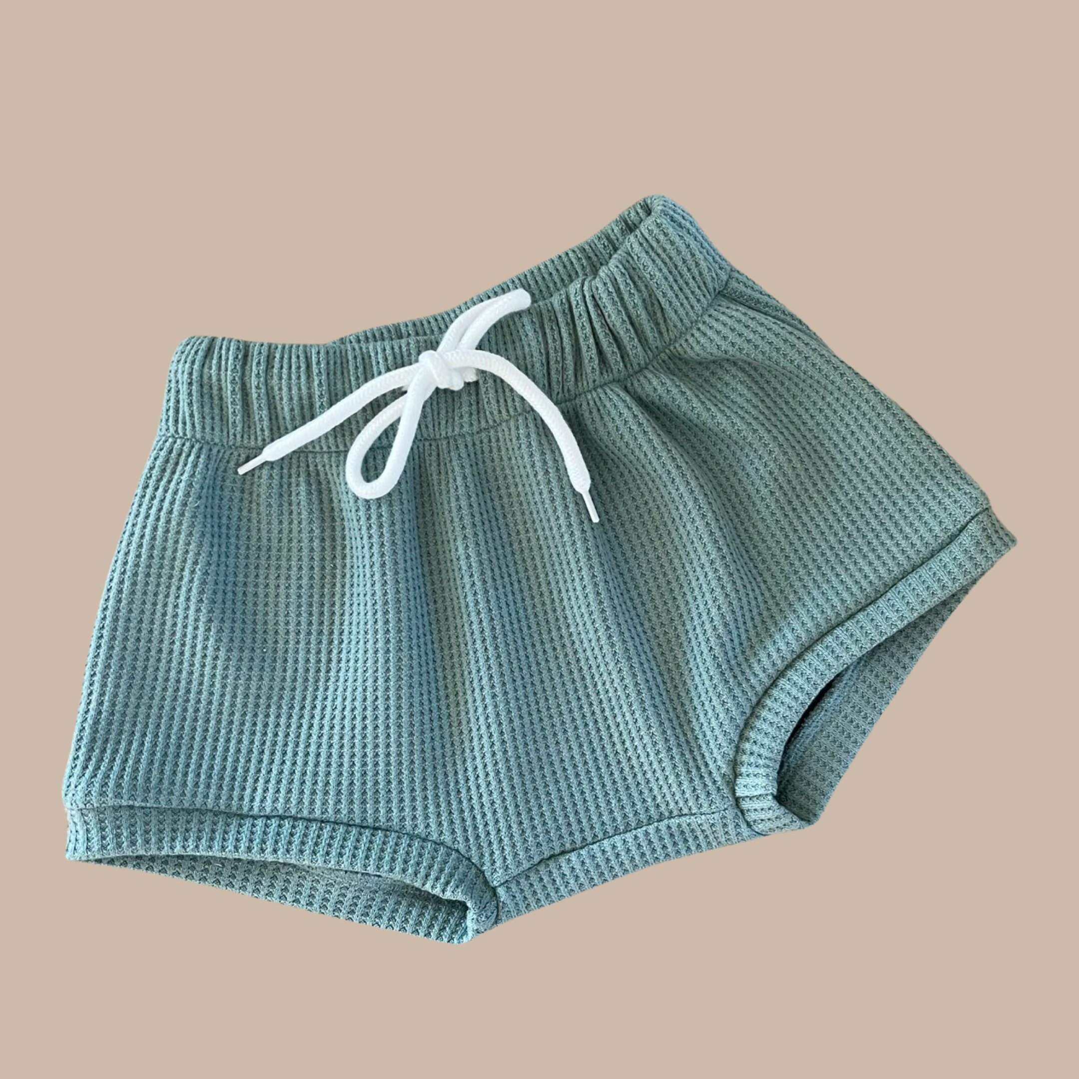 The Coby Shorts Kiwi by BOBBY G BABY WEAR, featuring a textured design in light green with an elastic waistband and white drawstring, provides unparalleled comfort against a plain taupe background.