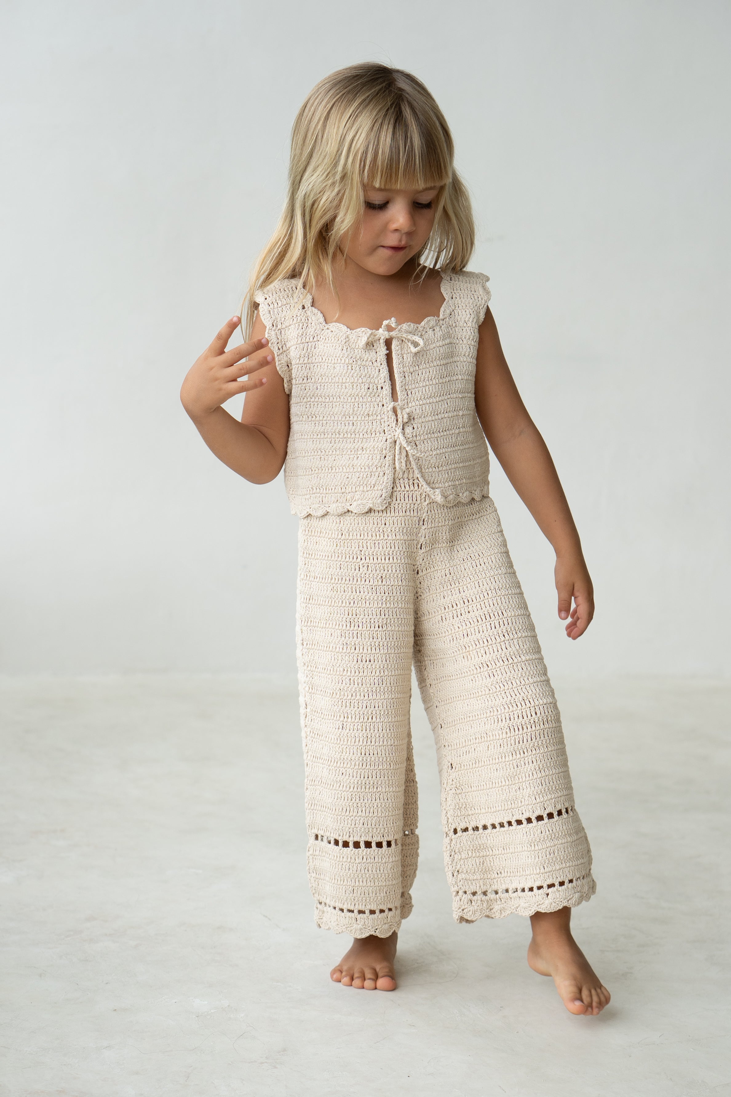 Young girl wearing the crochet vest in ecru with matching pants.