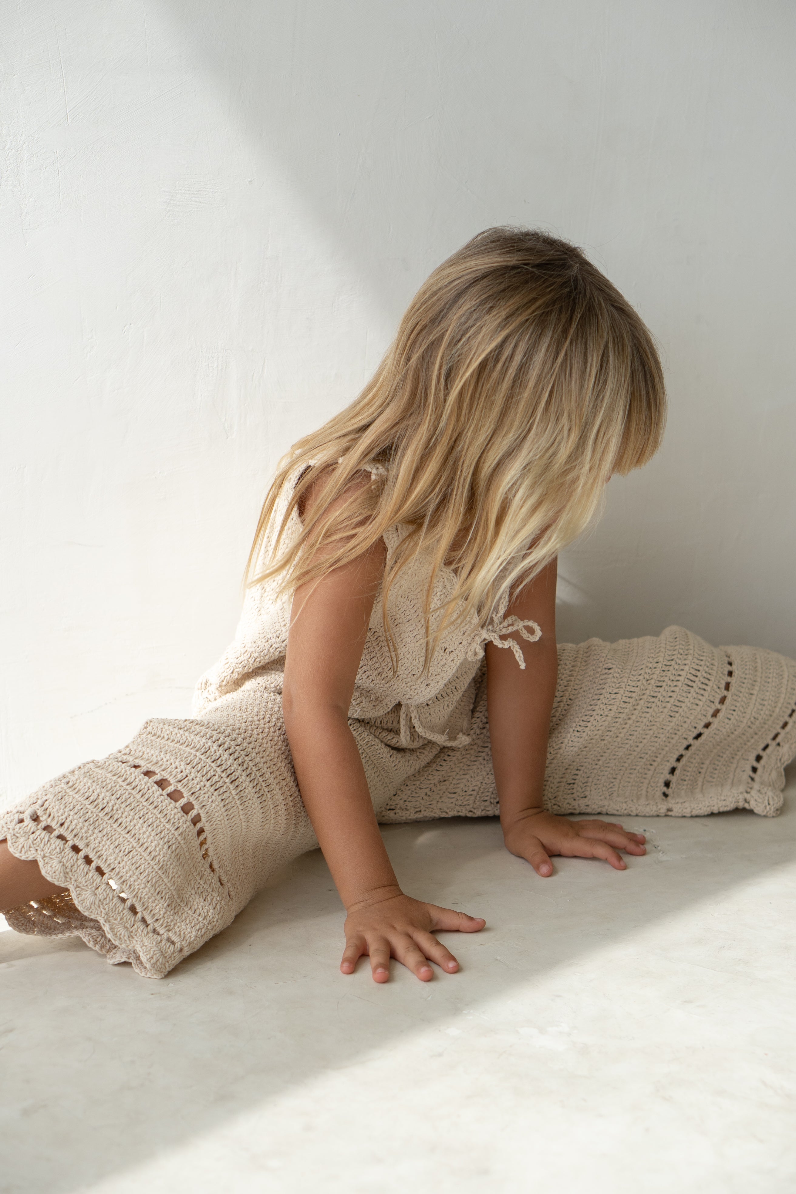 Young girl wearing the crochet pant in ecru with matching vest sitting in the splits.