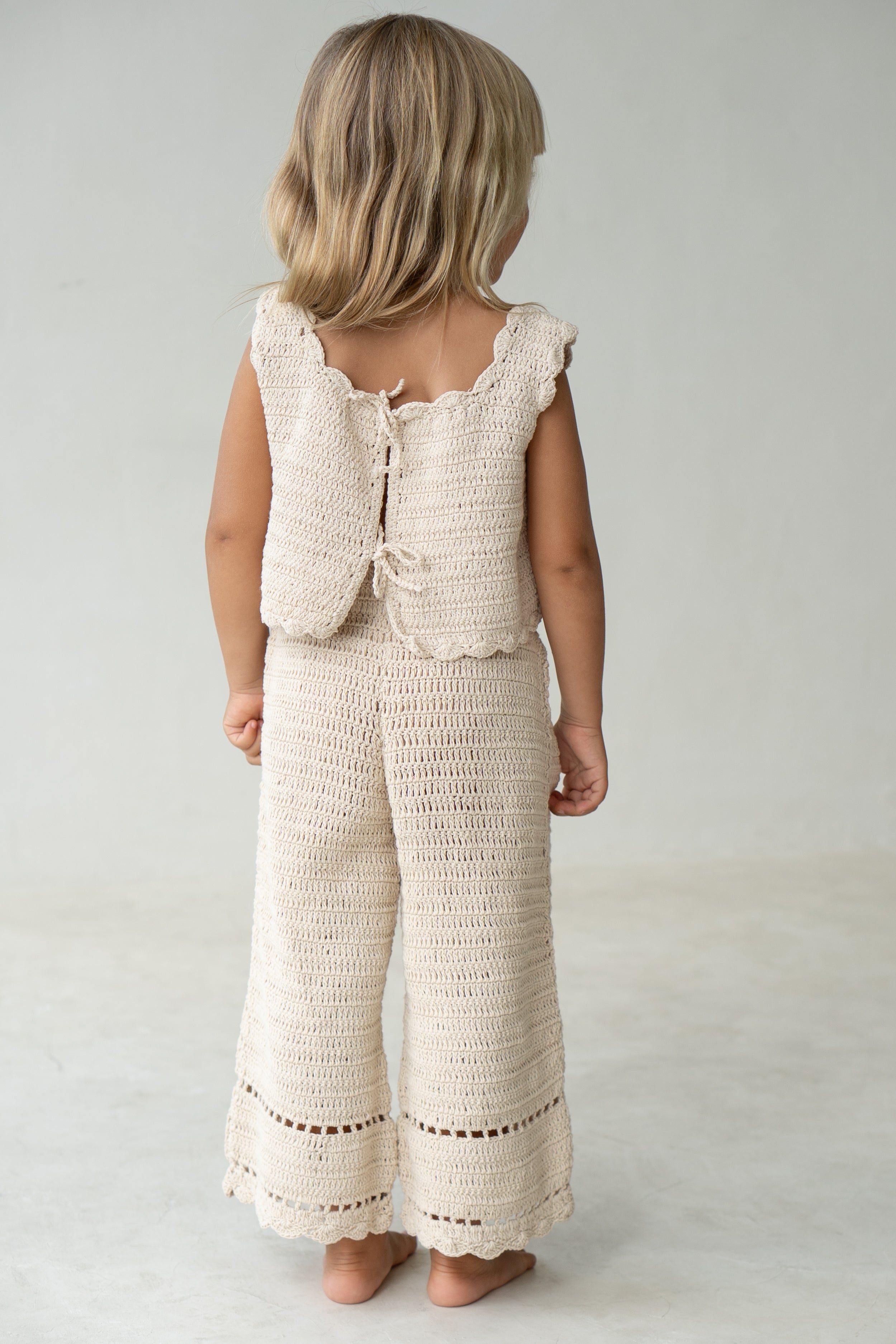 Young girl wearing the crochet vest in ecru with matching pants.