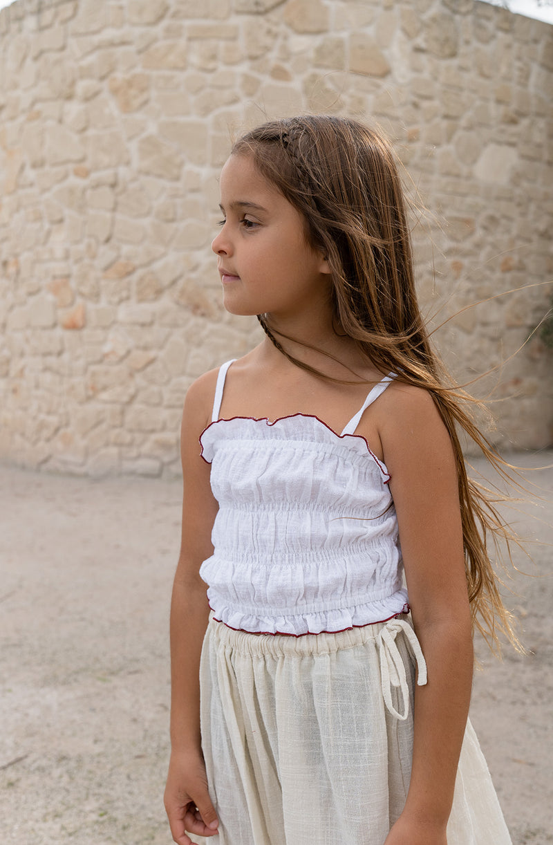 Girl wearing shirred white crop top, standing against a sandstone wall.