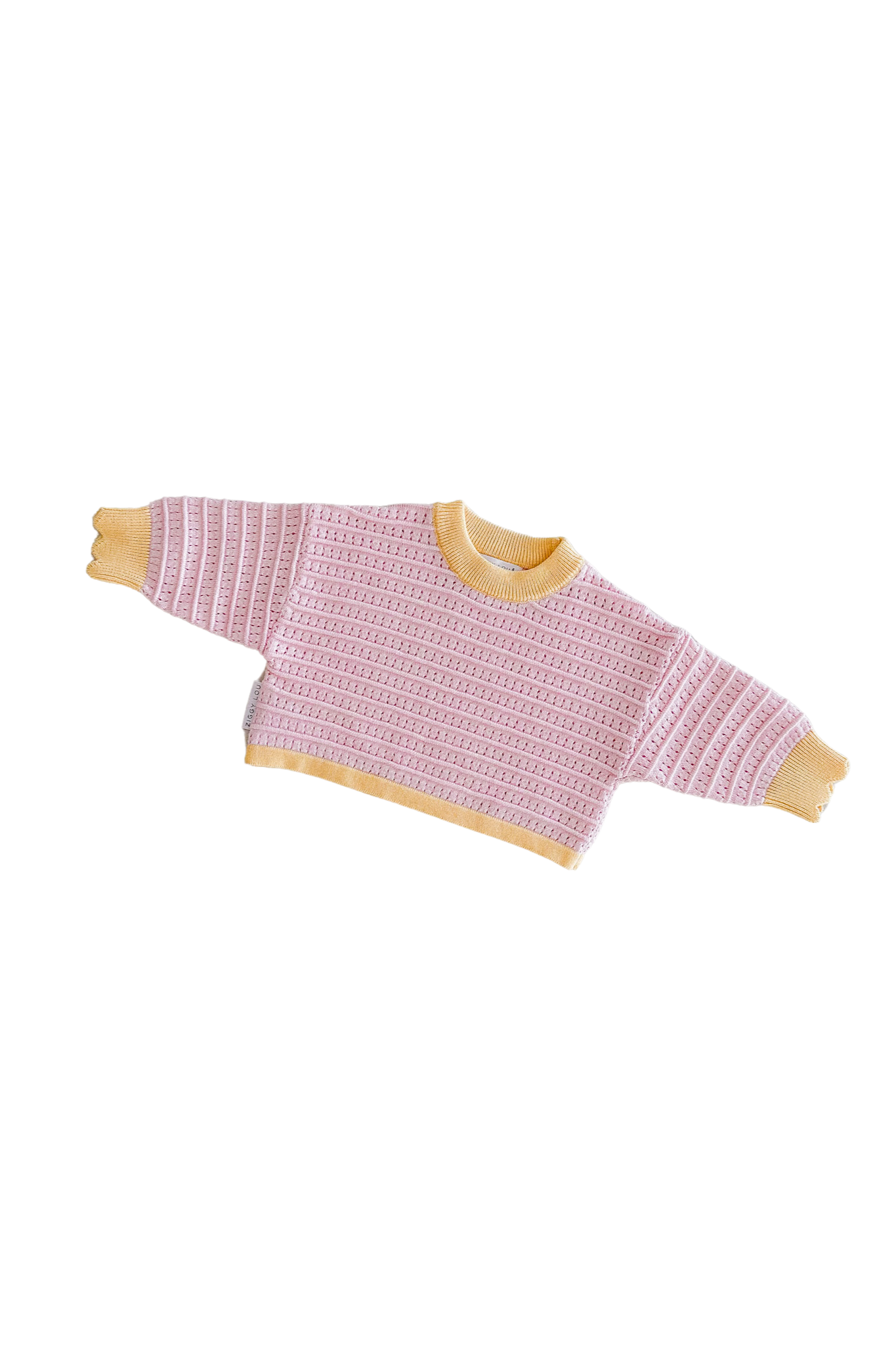 The Cropped Jumper Clementine by ZIGGY LOU, a 100% cotton sweater featuring a pink and white patterned body with yellow cuffs and collar, is elegantly displayed against a black background.