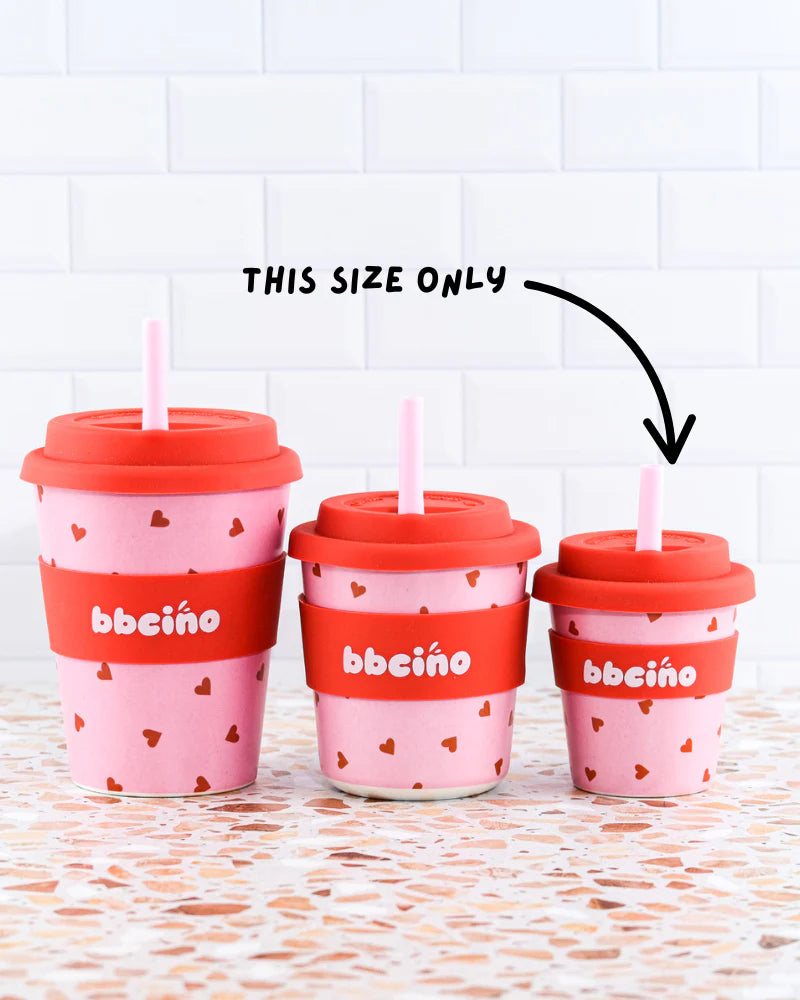 Three BBCINO "Reusable Babycino Cup 120ml Sweetheart" cups, featuring a pink design with red lids and heart patterns, sit on a speckled surface. An arrow points to the smallest cup with the label "THIS SIZE ONLY," indicating it is the only available size. These eco-friendly cups are an environmentally conscious alternative.