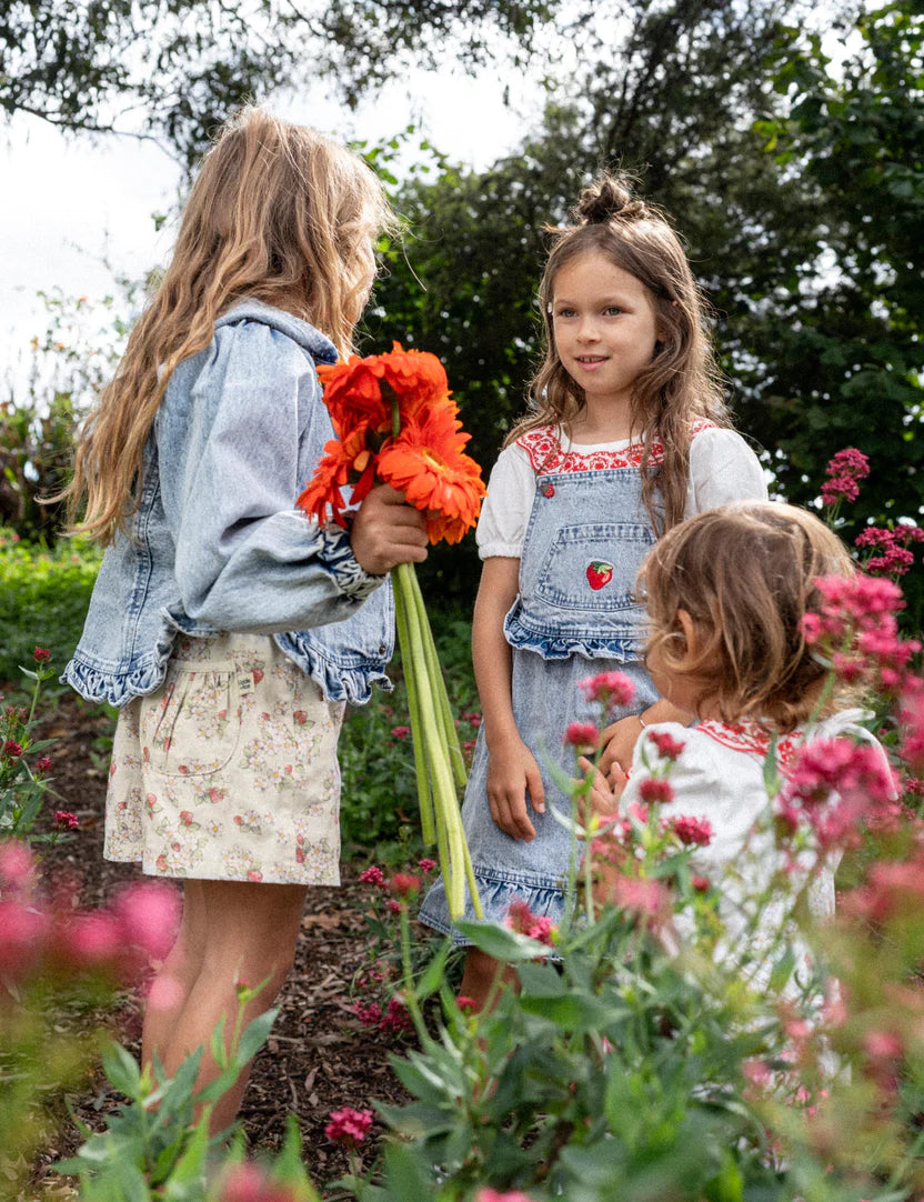 A young girl wearing the Pippa Strawberry Denim Pinafore Dress.