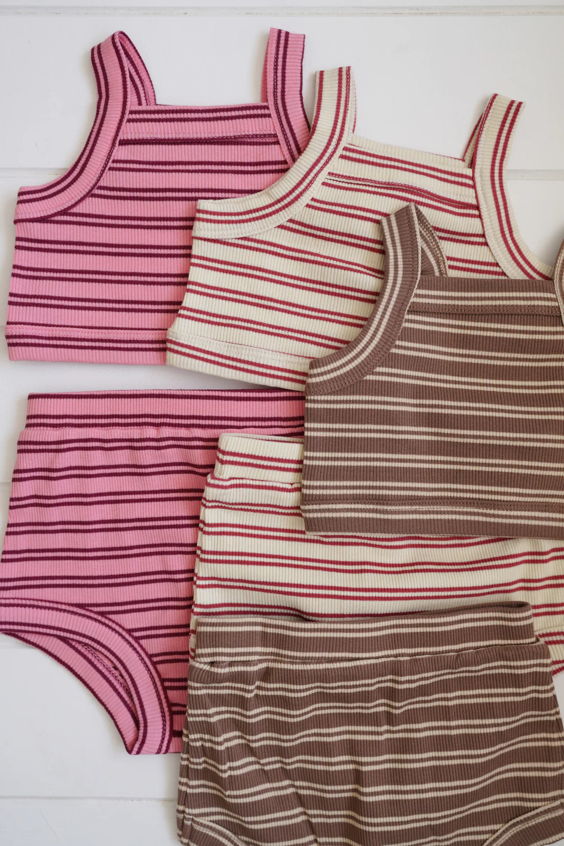 Introducing the Cleo Rib Set Pink/Red Stripe by MILKY DESIGNS: a collection of four playful outfits featuring ribbed cotton tank tops and matching shorts. Available in vibrant combinations of pink and white, cream and pink, pink and maroon, and brown and white stripes, each set is beautifully presented on a crisp white background.