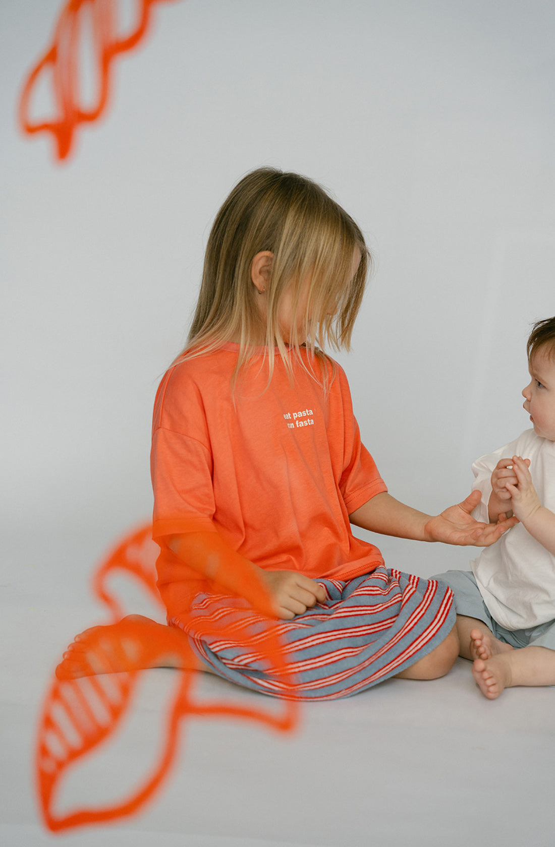 A young kid wearing the Lenn Peppa skirt and orange top playing with smaller kid.