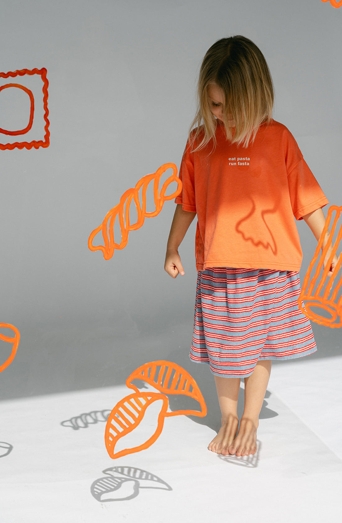 A young kid wearing the Lenn Peppa skirt with orange top..