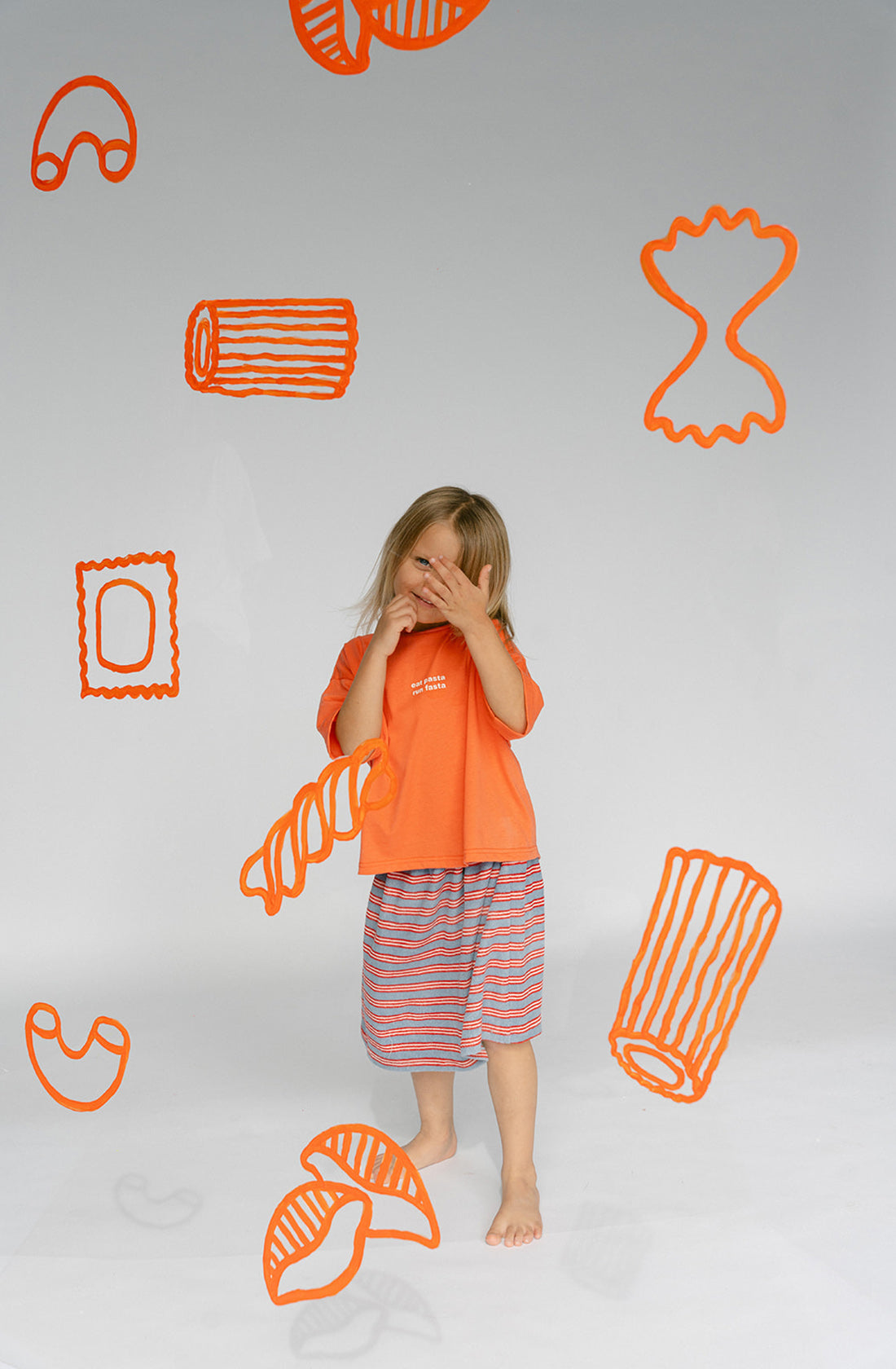 A young kid wearing the Lenn Peppa skirt with orange top with hands covering their face.