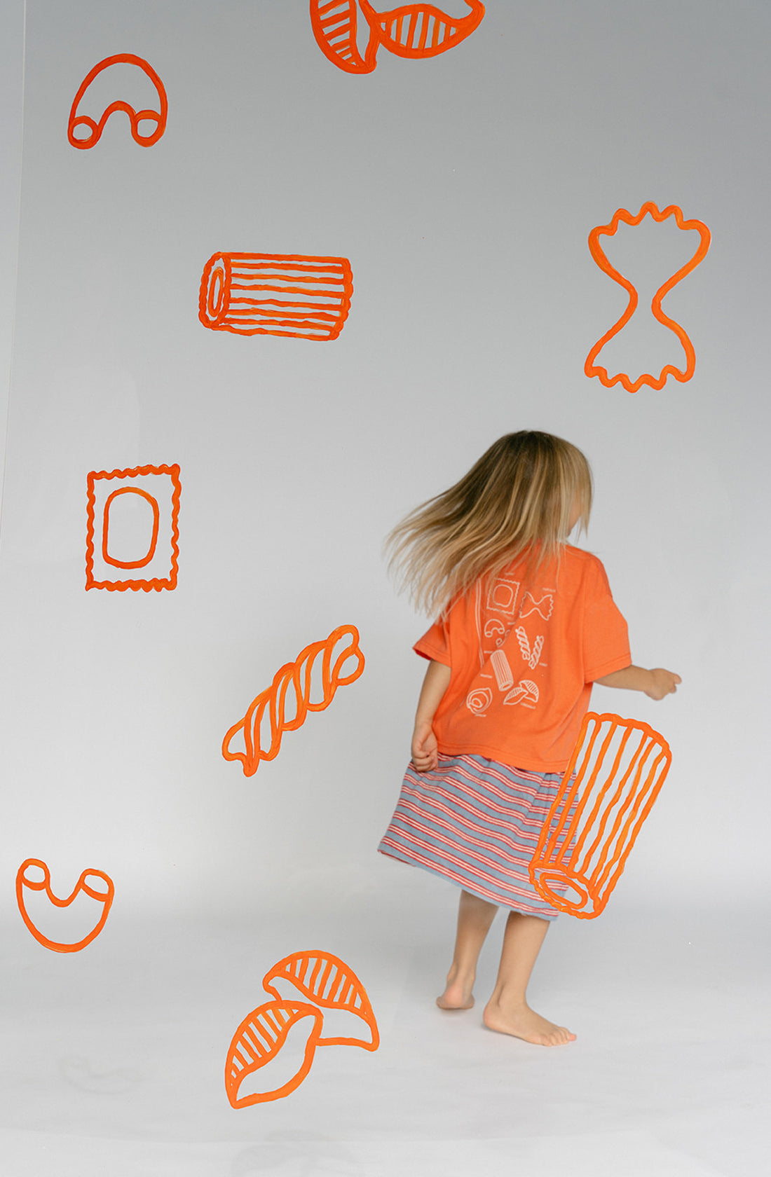 The back of a young kid wearing the Lenn pasta tee and striped skirt.