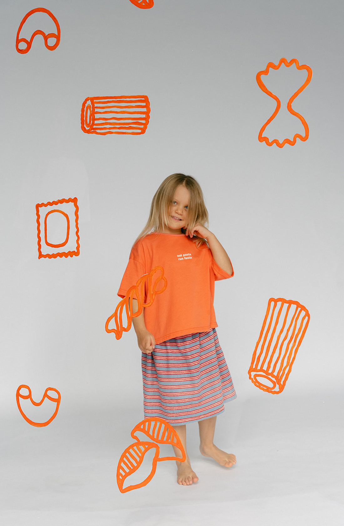 A young kid wearing the Lenn pasta tee and a striped skirt.