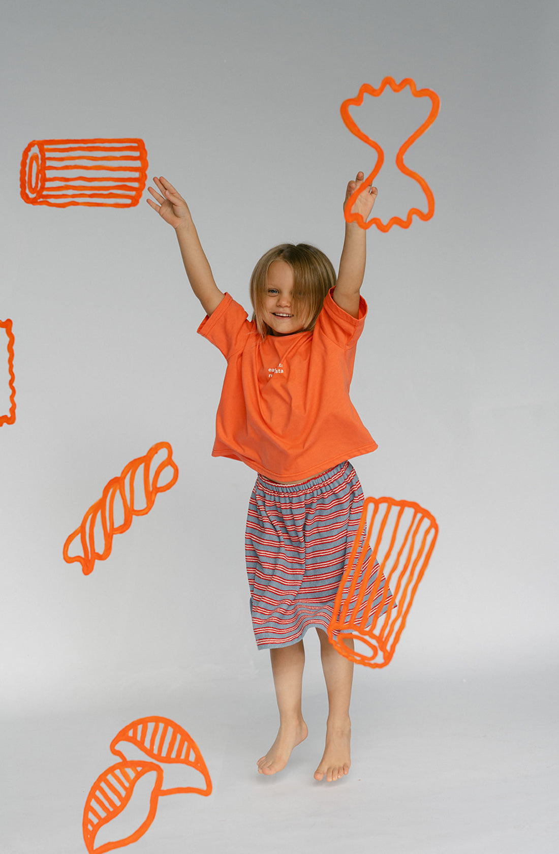 A young kid wearing the Lenn Peppa skirt with orange top with their hands in the air.