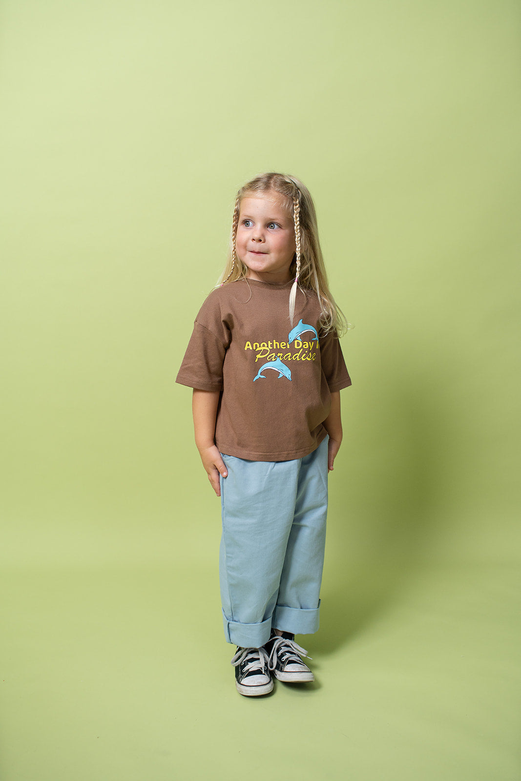 A young kid wearing the Lenn paradise tee  in brown with blue pants and shoes on.