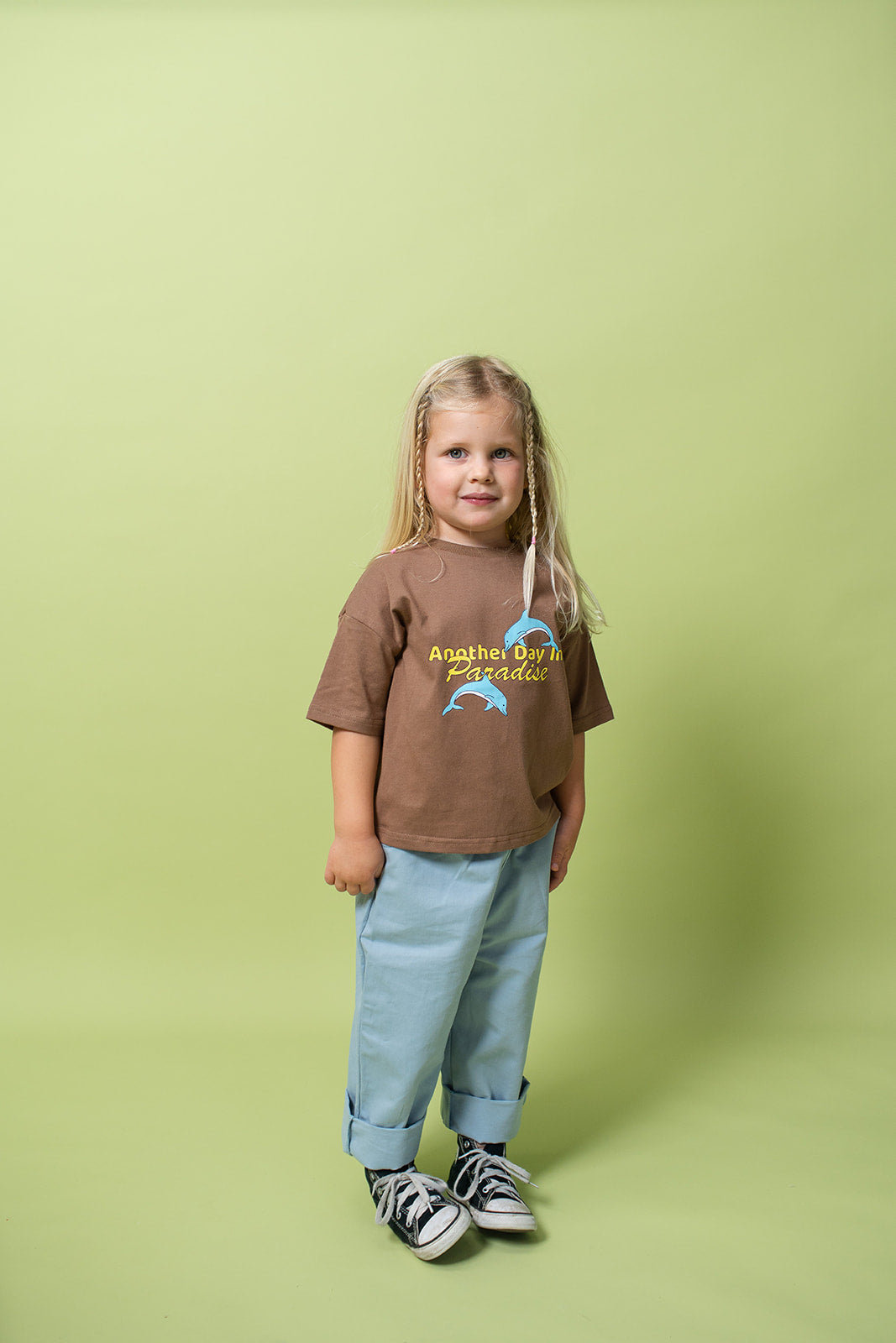 A young kid wearing the Lenn paradise tee  in brown. with blue pants and shoes on.