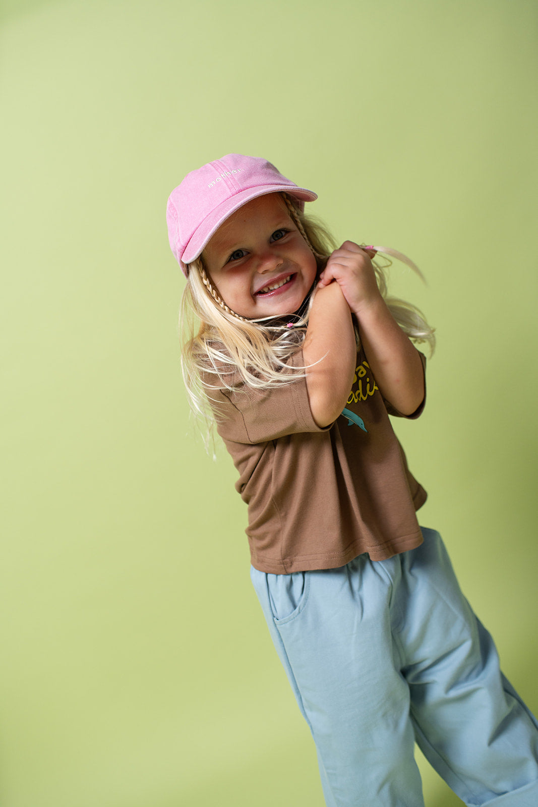 A young kid wearing the Lenn paradise tee  in brown with a pink hat on and blue pants.