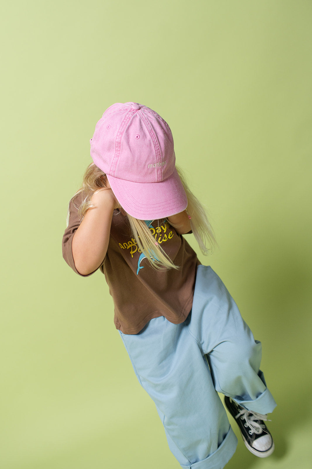 A young kid wearing the Lenn paradise tee  in brown with a pink hat and blue pants.