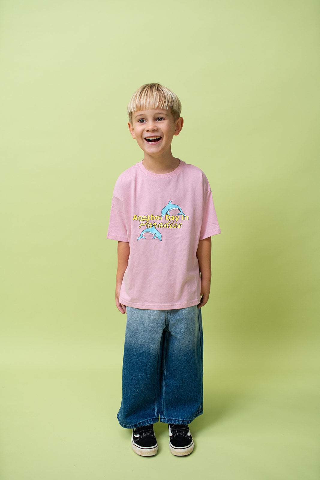 A young kid wearing the Lenn paradise tee in musk wearing jeans and black shoes.