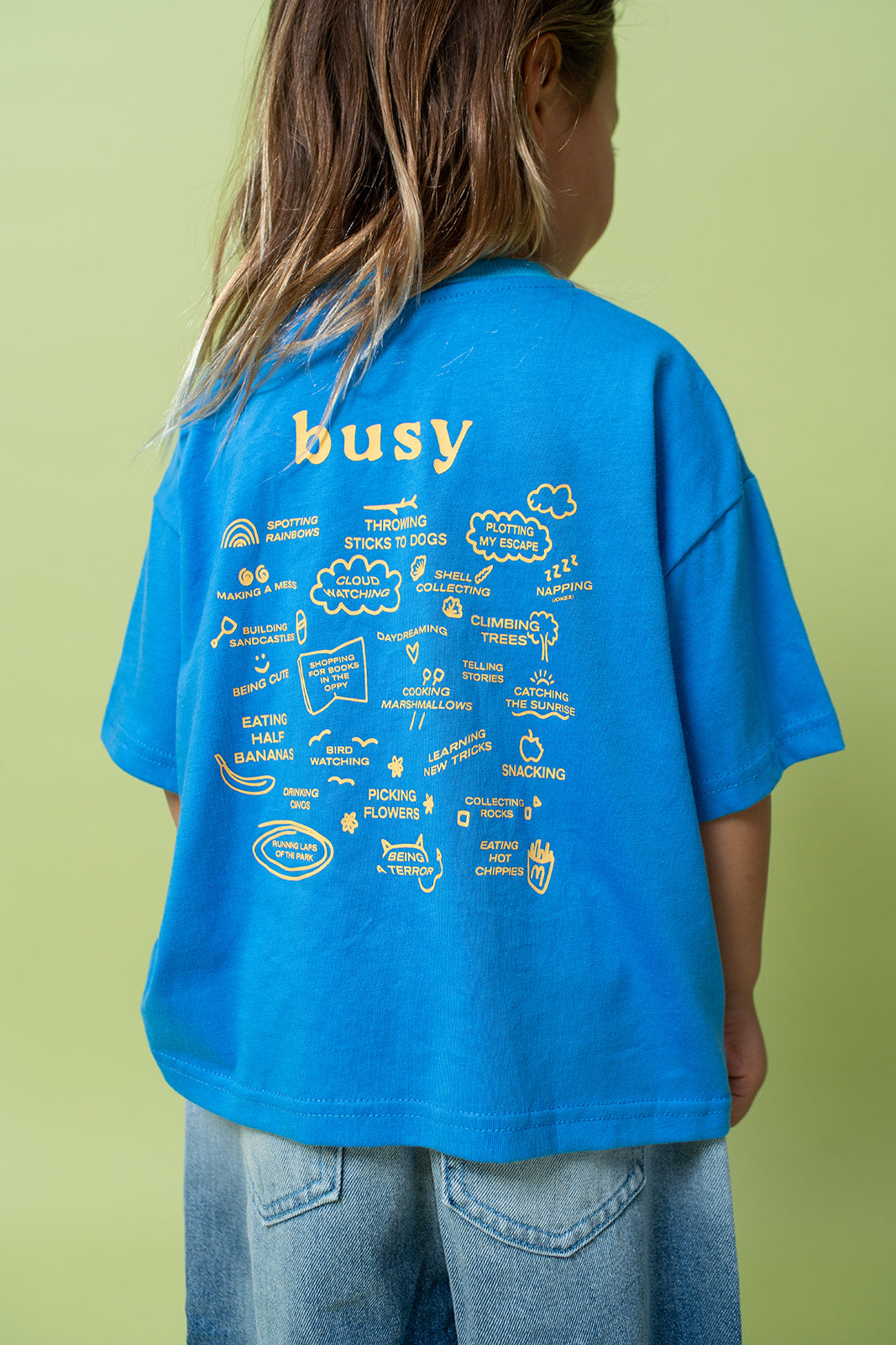 A young kid wearing the Lenn busy tee sunny shirt in blue from the back.