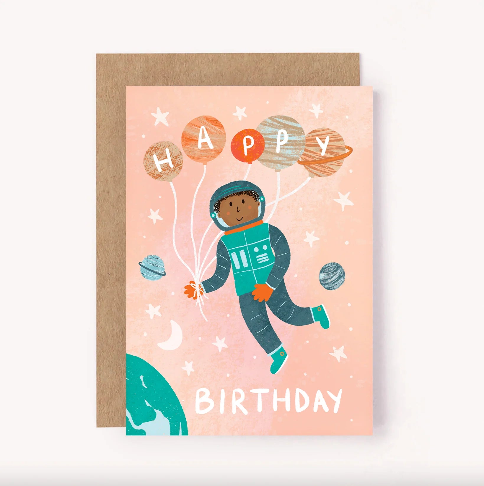 The LAUREN SISSONS STUDIO’s "Birthday Greeting Card 'Astronaut'" showcases an astronaut drifting in a pink outer space backdrop adorned with stars and planets. The astronaut holds balloons forming the word "Happy," while "Birthday" is printed below in white. Accompanied by a recycled paper envelope, the design also includes illustrations of Earth and a crescent moon.