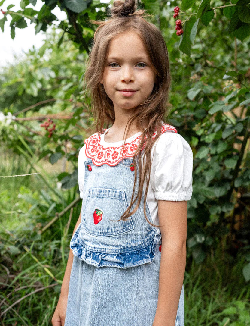 A young girl wearing the Pippa Strawberry Denim Pinafore Dress.