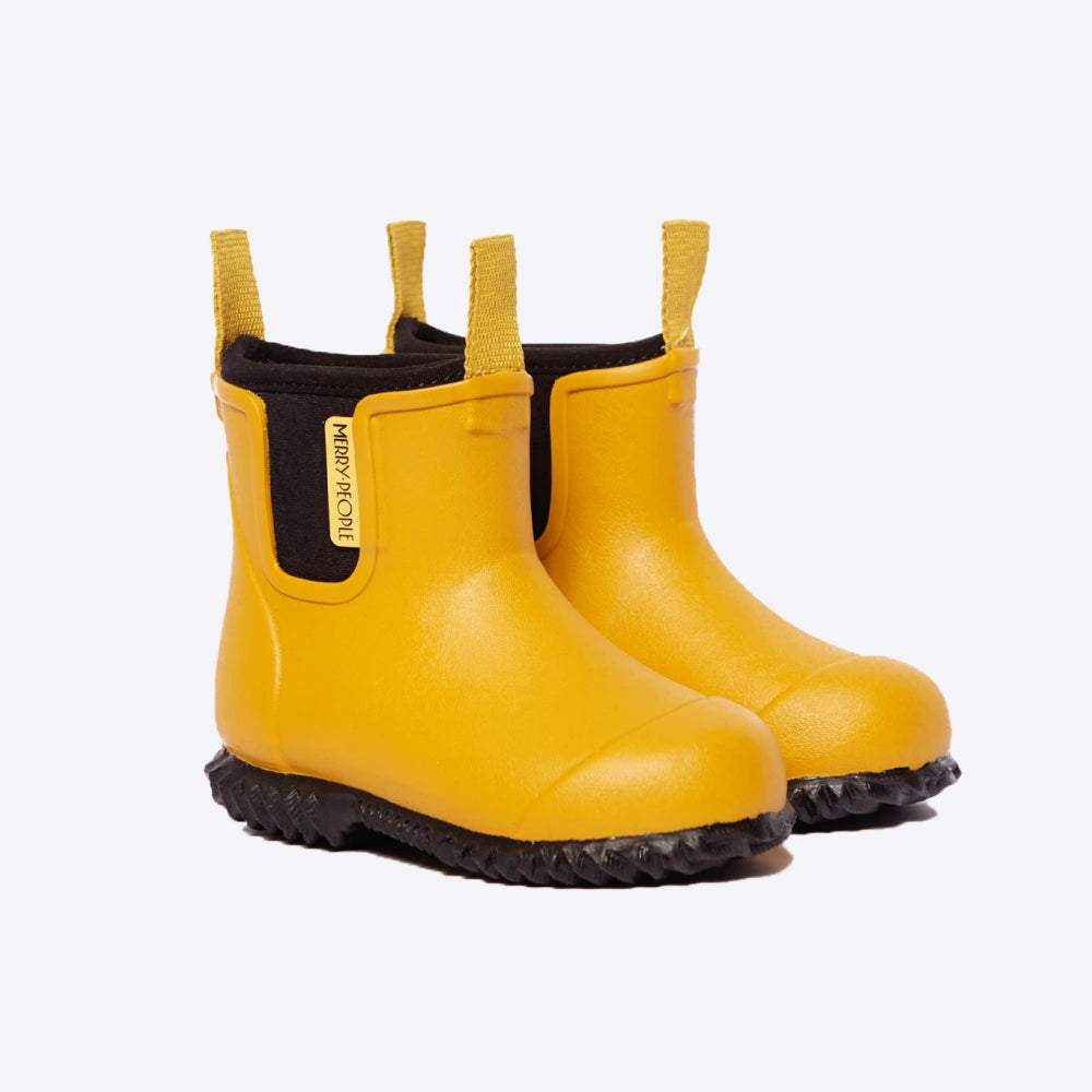 The Merry People Bobbi Kids Gumboot in Mustard Yellow features elastic sides, black soles, and pull tabs. These 100% waterproof boots offer vegan arch support and have a small label on the side, standing against a plain white background.