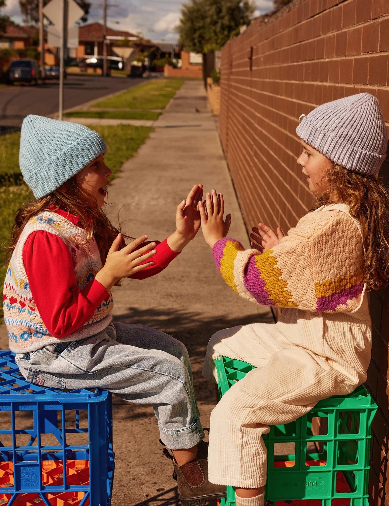 Two girls sitting down clapping hands wearing the GOLDIE + ACE  Wool Beanie Sky and lilac.