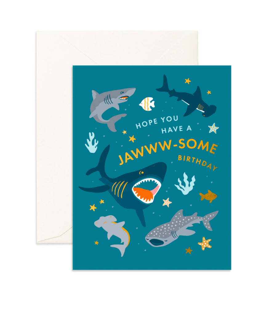 The Jawww-Some Birthday Greeting Card by FOX & FALLOW showcases an underwater theme with illustrated sharks and fish on a teal background. The card is accented with gold metallic foil and features the text "Hope you have a jawww-some birthday" in yellow and white letters. The foil greeting card comes paired with a white envelope.