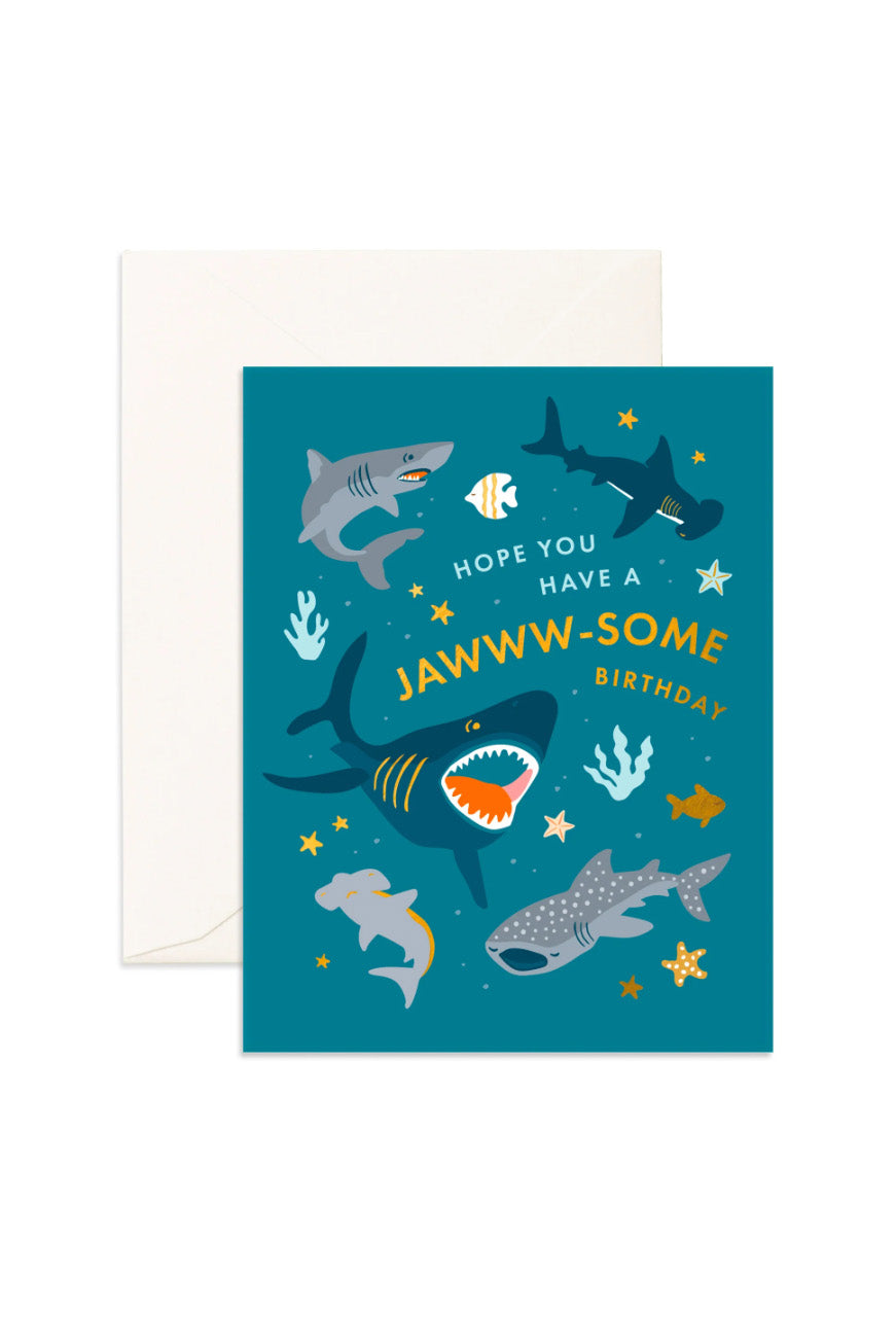 Introducing the FOX & FALLOW Jawww-Some Birthday Greeting Card: This vibrant foil card showcases whimsical illustrations of sharks, starfish, and sea plants set against a teal backdrop with shimmering gold metallic accents. The playful message, "Hope you have a JAWWW-SOME birthday," is prominently displayed. Comes complete with a white envelope for your convenience.