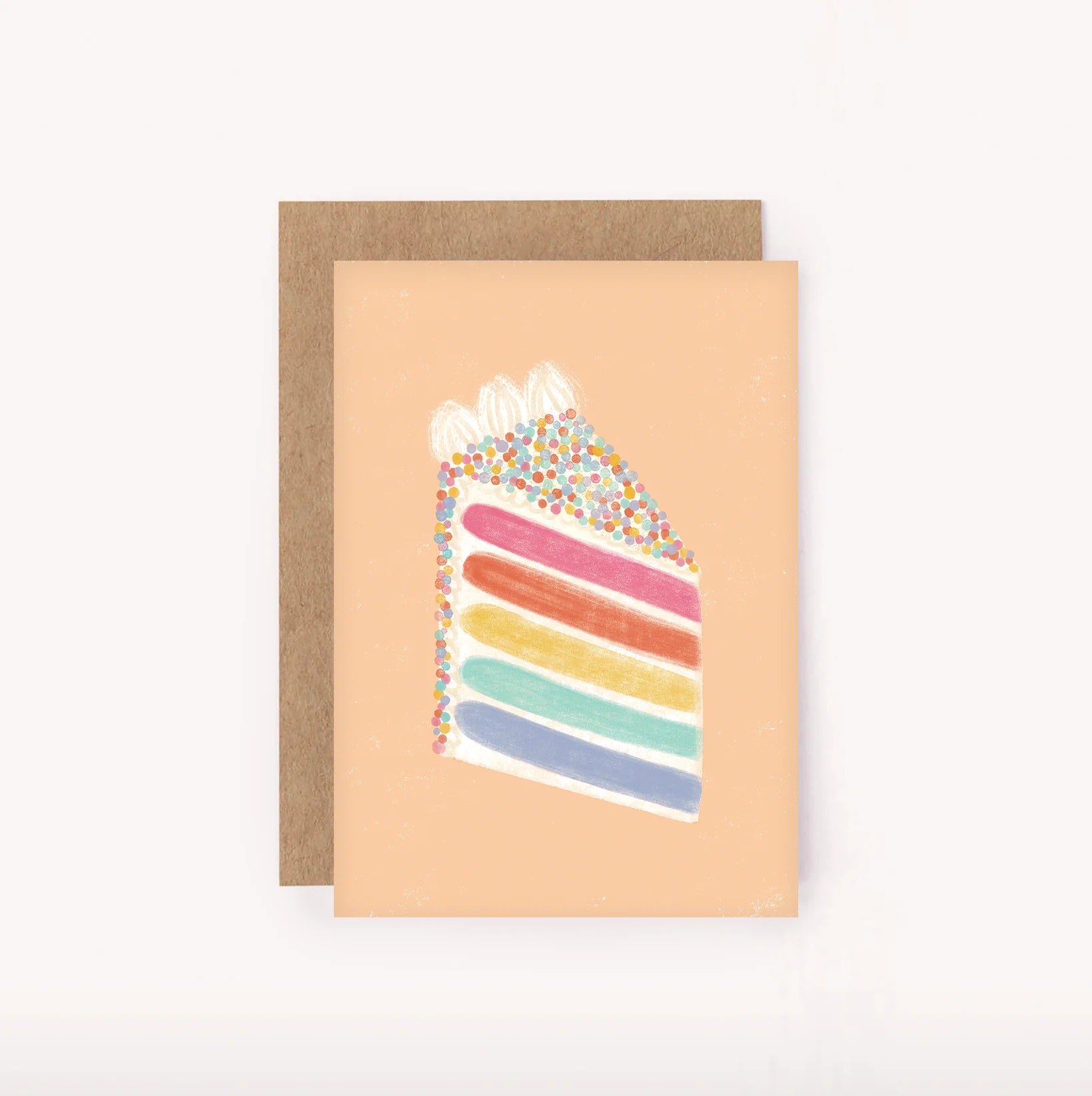 The Rainbow Cake Mini Card by LAUREN SISSONS STUDIO showcases an illustration of a slice of rainbow cake with multicolored layers and sprinkles on top. It features a peach-colored background and comes with a plain brown envelope crafted from recycled paper.