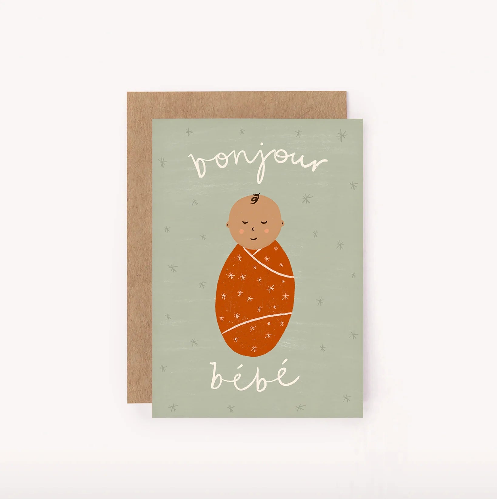 The "Bonjour Bebe Mini Card - New Baby" by LAUREN SISSONS STUDIO is a gender-neutral baby card that features an illustration of a newborn wrapped in an orange blanket. Set against a light green background adorned with small star patterns, the card also includes a brown envelope. The phrase "Bonjour bébé" is elegantly written in white cursive font, making it perfect for any mini baby shower.