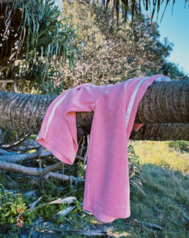 A Ziggy Zaza ~ Twin Stripe Terry Pant Pink from ZIGGY ZAZA draped over a tree branch in a natural setting, surrounded by greenery. Sunlight dapples the scene, creating a serene and relaxing atmosphere.