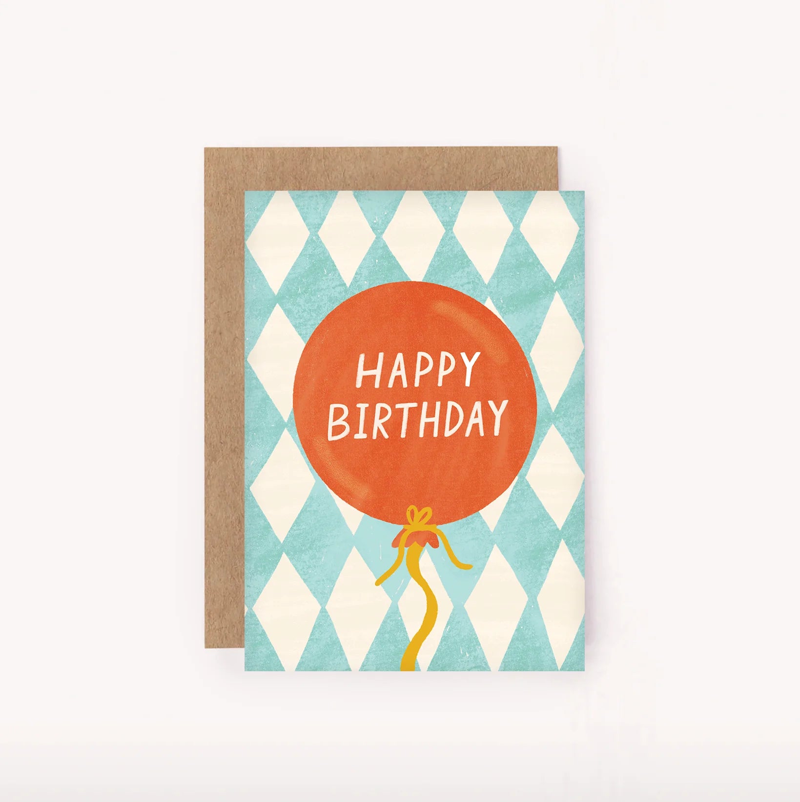 The Birthday Balloon Mini Card by LAUREN SISSONS STUDIO showcases a teal and white diamond pattern background adorned with an orange balloon that reads "Happy Birthday." Made from recycled paper, the design is complemented by a yellow ribbon hanging from the balloon. A brown envelope is slightly visible behind the card.