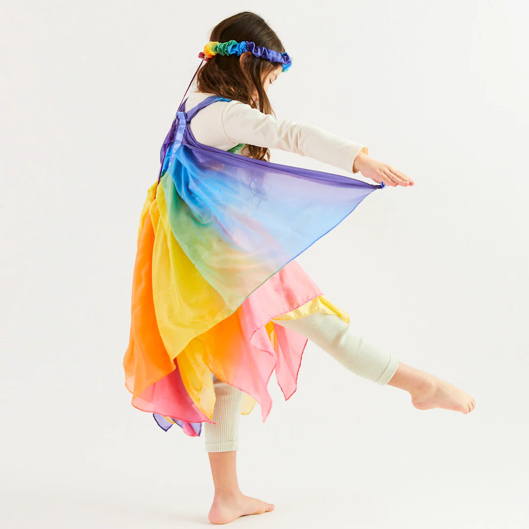 A child, delighting in the magic of dress-up, spins gracefully in a pair of SARAH'S SILKS Rainbow Wings, their vibrant blues, greens, yellows, and pinks creating a stunning rainbow effect against a plain white background.