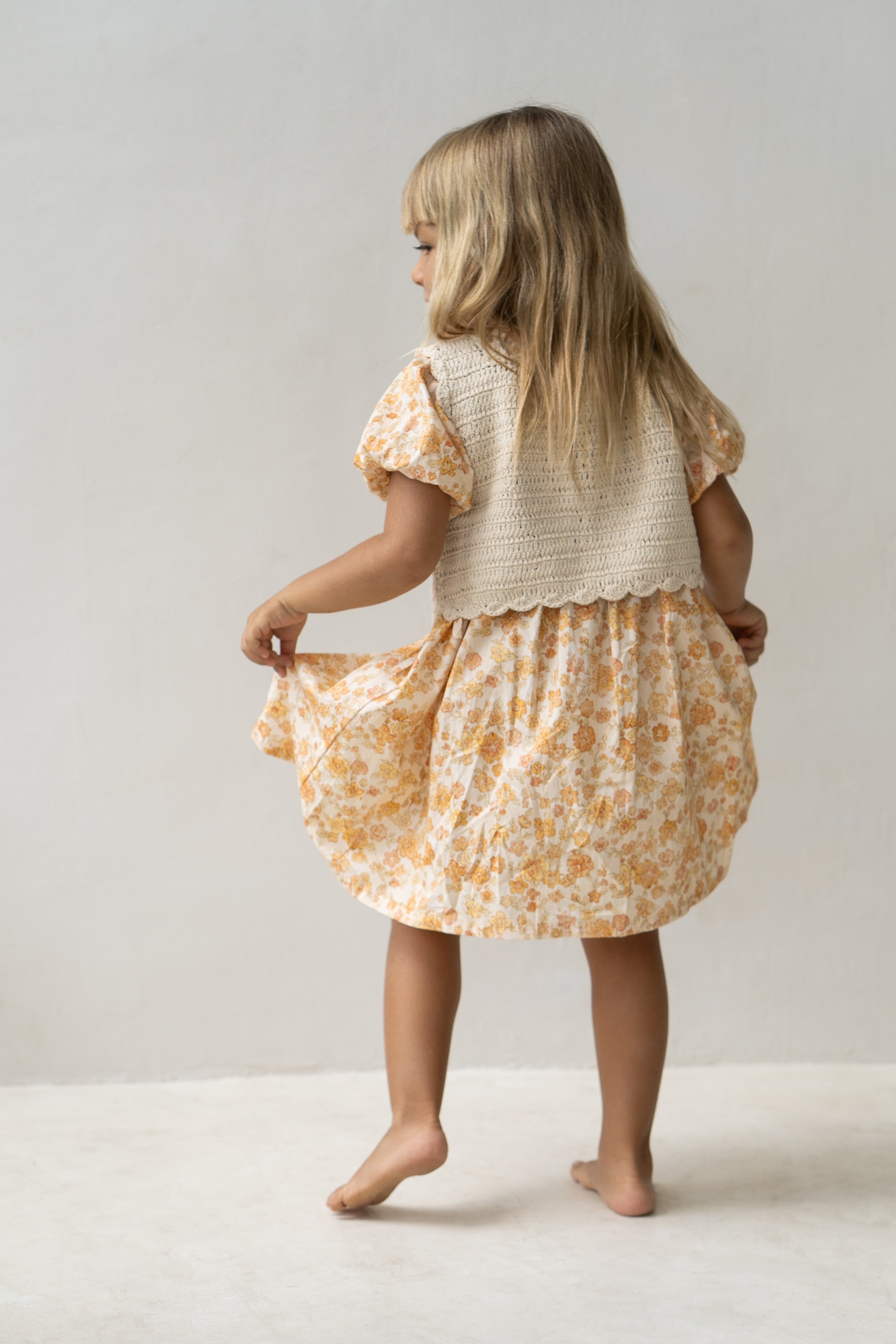 Young girl wearing the florence dress in buttercup and a beige vest..