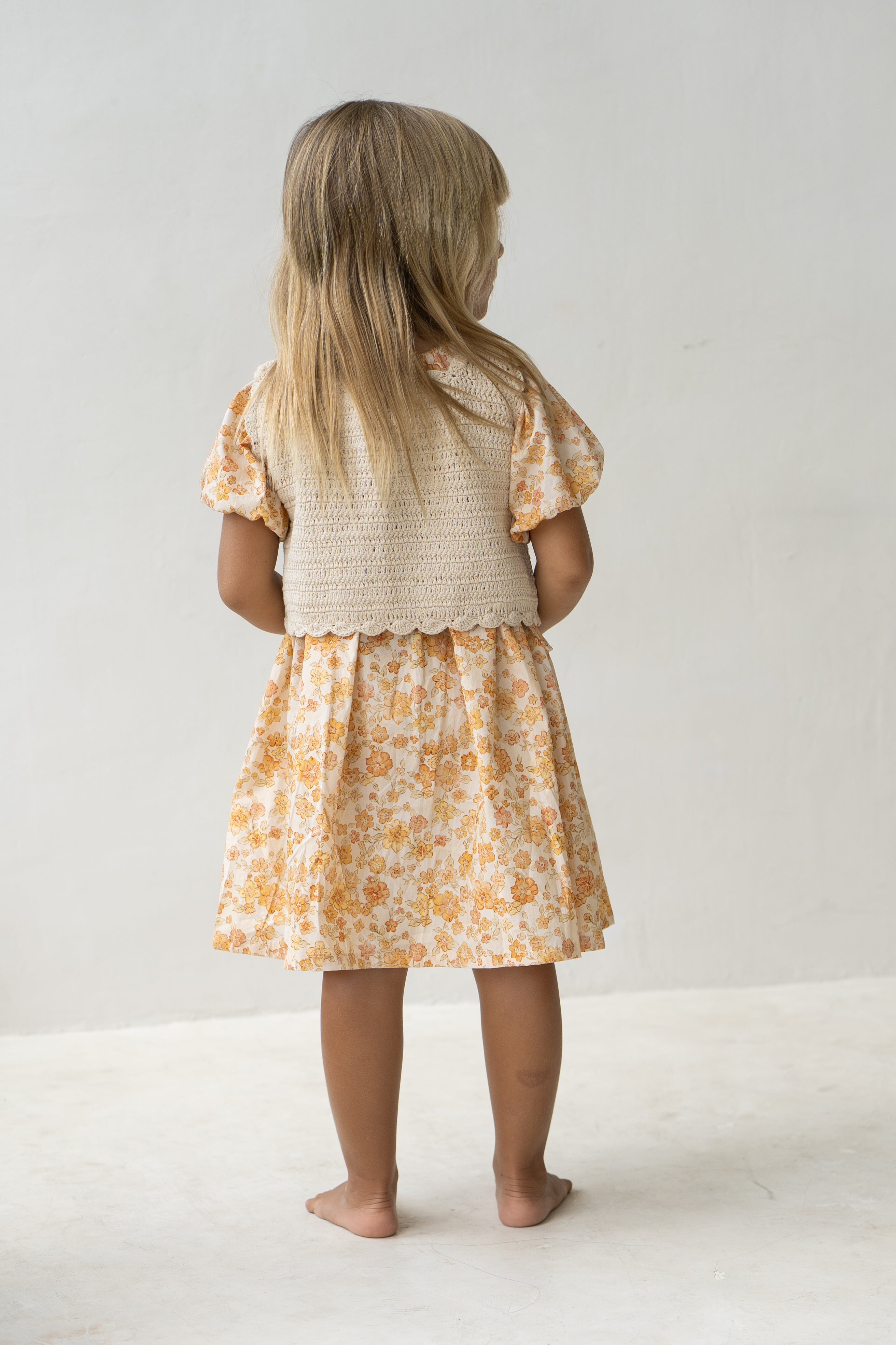 Young girl wearing the florence dress in buttercup and a beige vest.