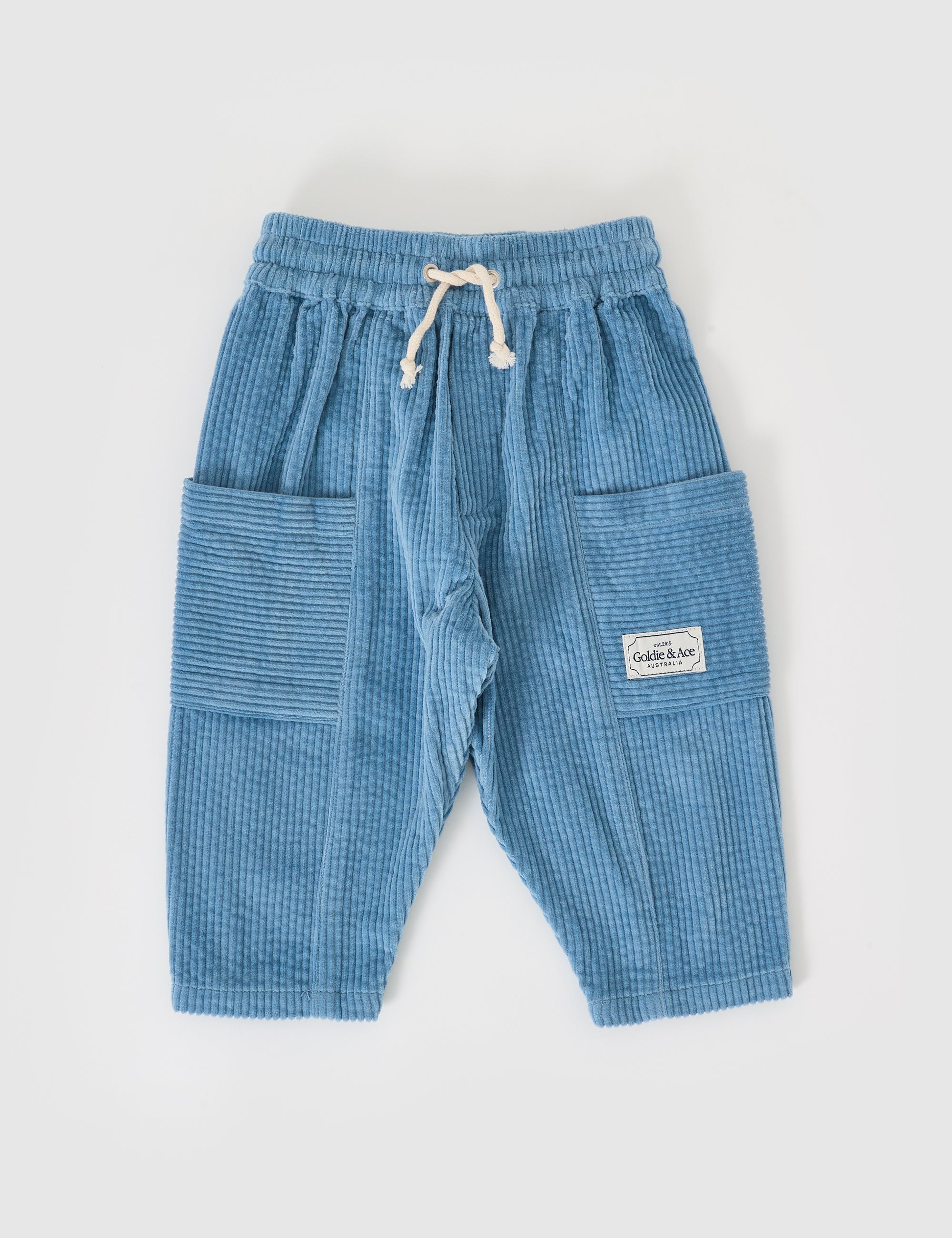 The Goldie + Ace Kit Corduroy Pocket Pant in Duck Egg is crafted from blue cotton for children, featuring an elastic waistband, drawstring, two large side pockets with a small white label on the right one, and a wide-leg style. Presented on a flat white background by GOLDIE + ACE.