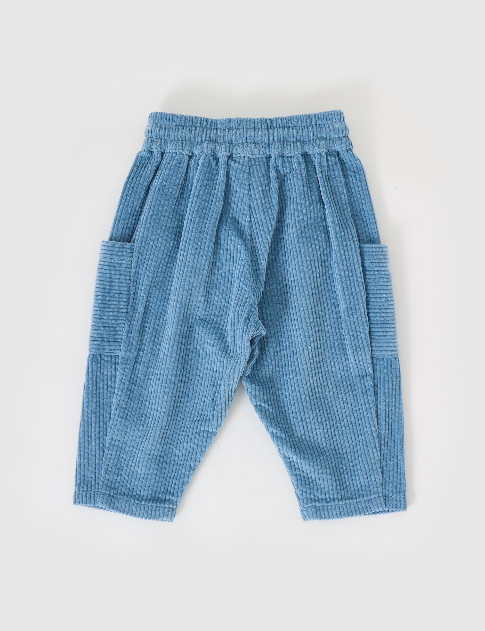 The "Goldie + Ace ~ Kit Corduroy Pocket Pant Duck Egg" by GOLDIE + ACE are light blue, wide-leg, cotton corduroy trousers for children. They feature an elastic waistband and two oversized side pockets, displayed on a white background.