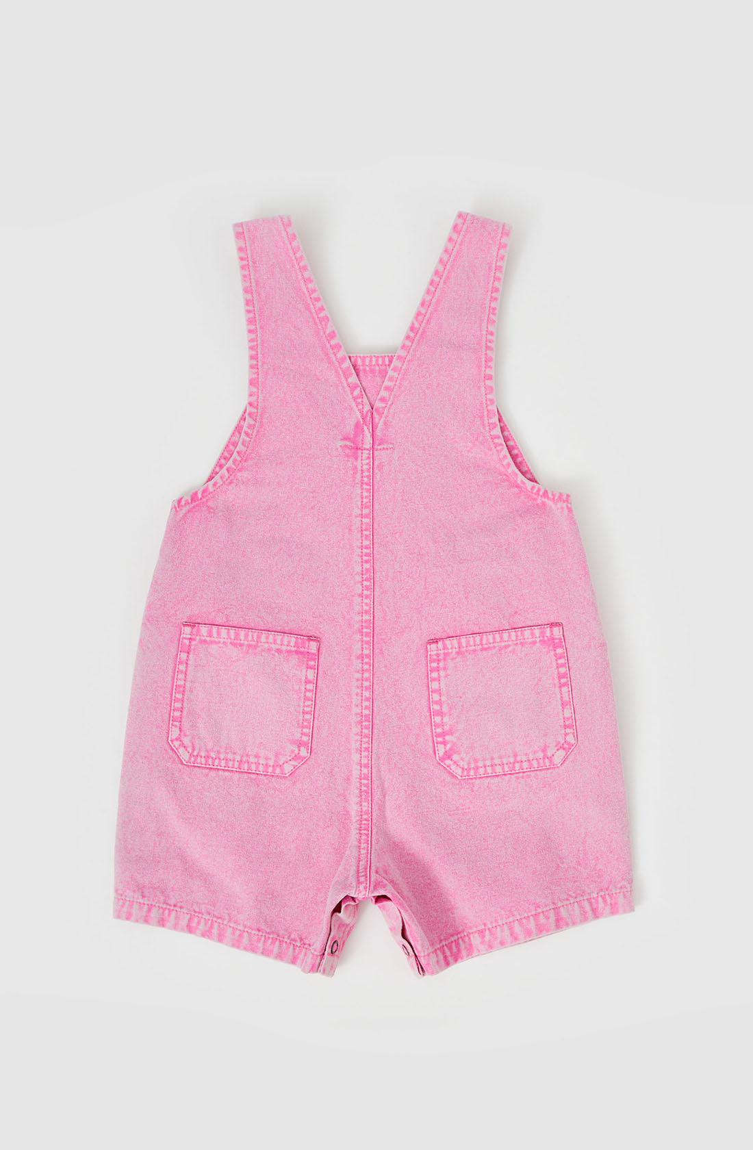 The Burton Vintage Washed Denim Overalls by GOLDIE + ACE are pink denim rompers for toddlers, featuring a sleeveless design with two front pockets and buttons at the crotch. These rompers also have a V-shaped back with crossed, adjustable shoulder straps.