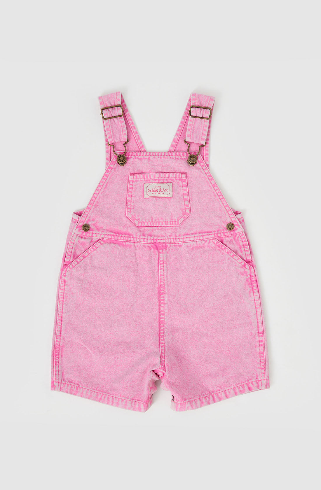 The Burton Vintage Washed Denim Overalls by GOLDIE + ACE feature an adjustable shoulder strap and metal buckles. The front has a small chest pocket with a decorative label, side waist pockets, short pant legs, and convenient leg snaps.