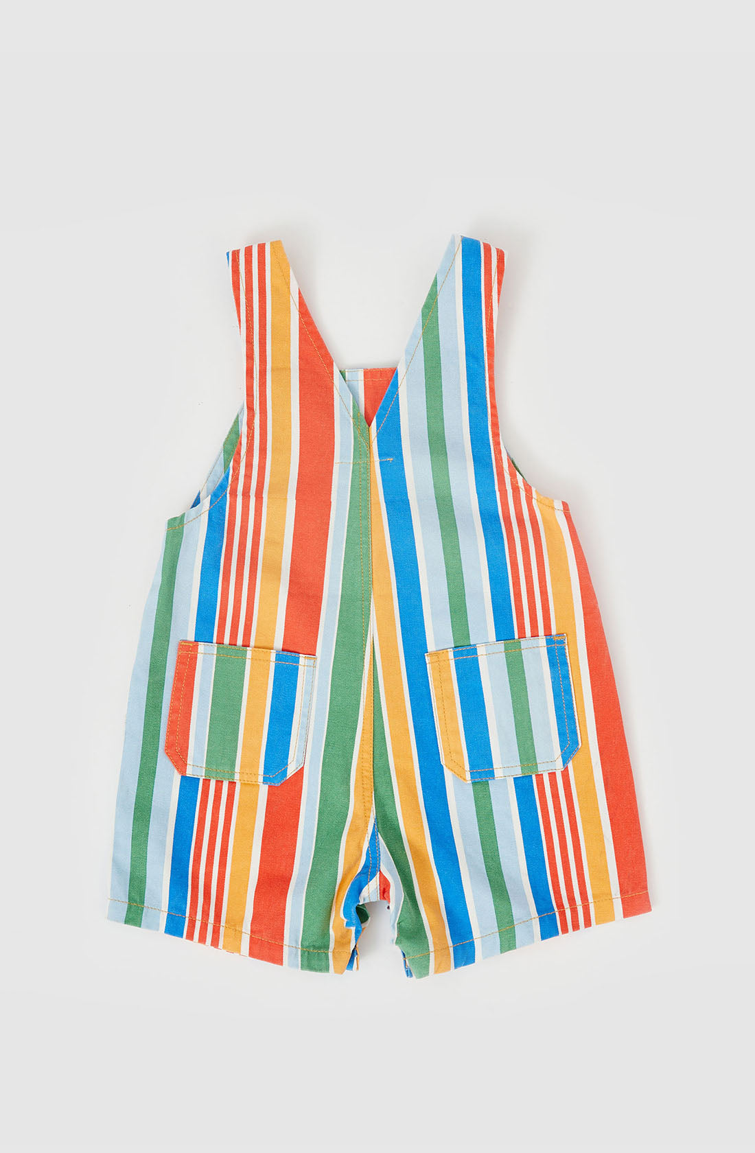 The Burton Striped Denim Overalls by GOLDIE + ACE are a vibrant pair of baby overalls designed with rainbow vertical stripes in red, orange, yellow, green, blue, and turquoise. These sleeveless overalls feature adjustable straps and leg snaps for easy changes, along with two front pockets that showcase matching colorful stripes.