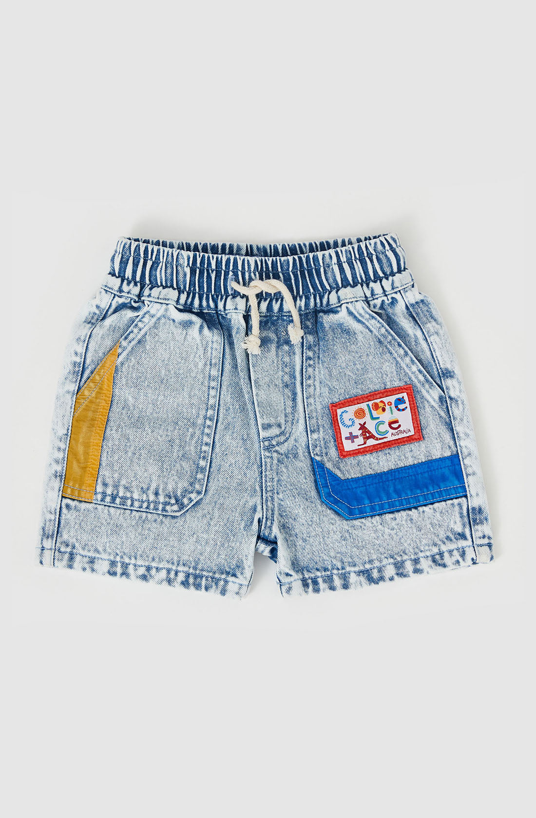 The Noah Colour Pop Denim Shorts by GOLDIE + ACE are light blue with a functional drawcord and elastic waistband. They feature colorful patches: a yellow pocket on the left and a blue pocket with a multicolored patch on the right. The fabric has a slightly worn look, adding to their relaxed charm.