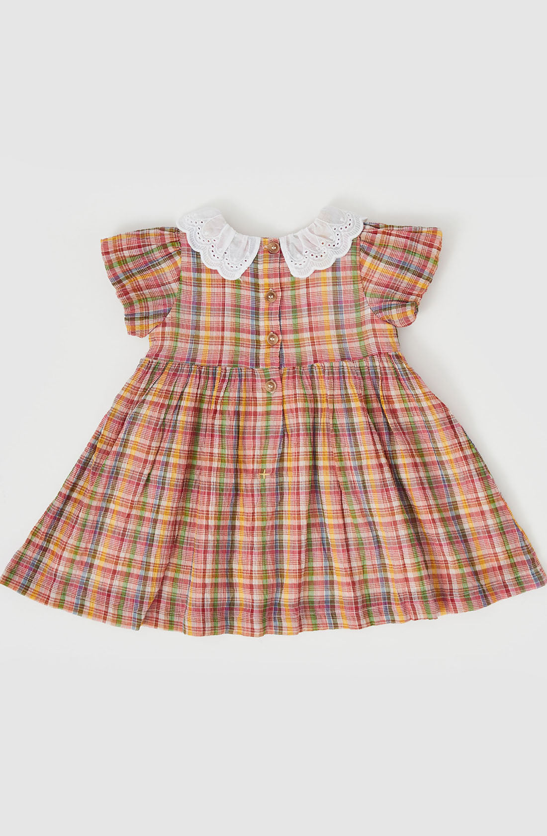 The Flo Smocked Dress by GOLDIE + ACE is a delightful children's dress showcasing a vibrant Maroon Rainbow check pattern with hues of red, orange, yellow, green, and blue. It features short, ruffled sleeves, a white lace collar, and a front button placket. The smocked bodice and pleated skirt contribute to its full, flared appearance.