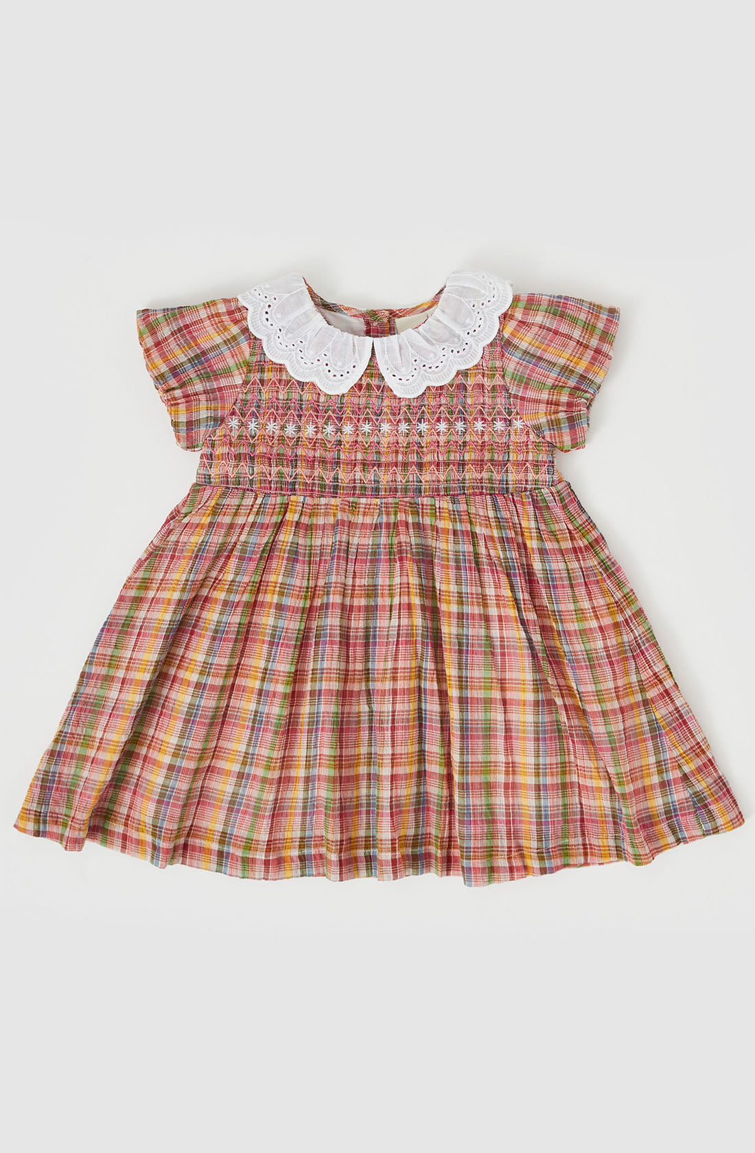 The Flo Smocked Dress by GOLDIE + ACE is a child's plaid dress featuring short, capped sleeves and a white, scalloped collar. Decorated with a maroon rainbow check pattern, its smocked bodice adds charming detail across the chest, creating a slightly gathered and flared effect toward the hem.