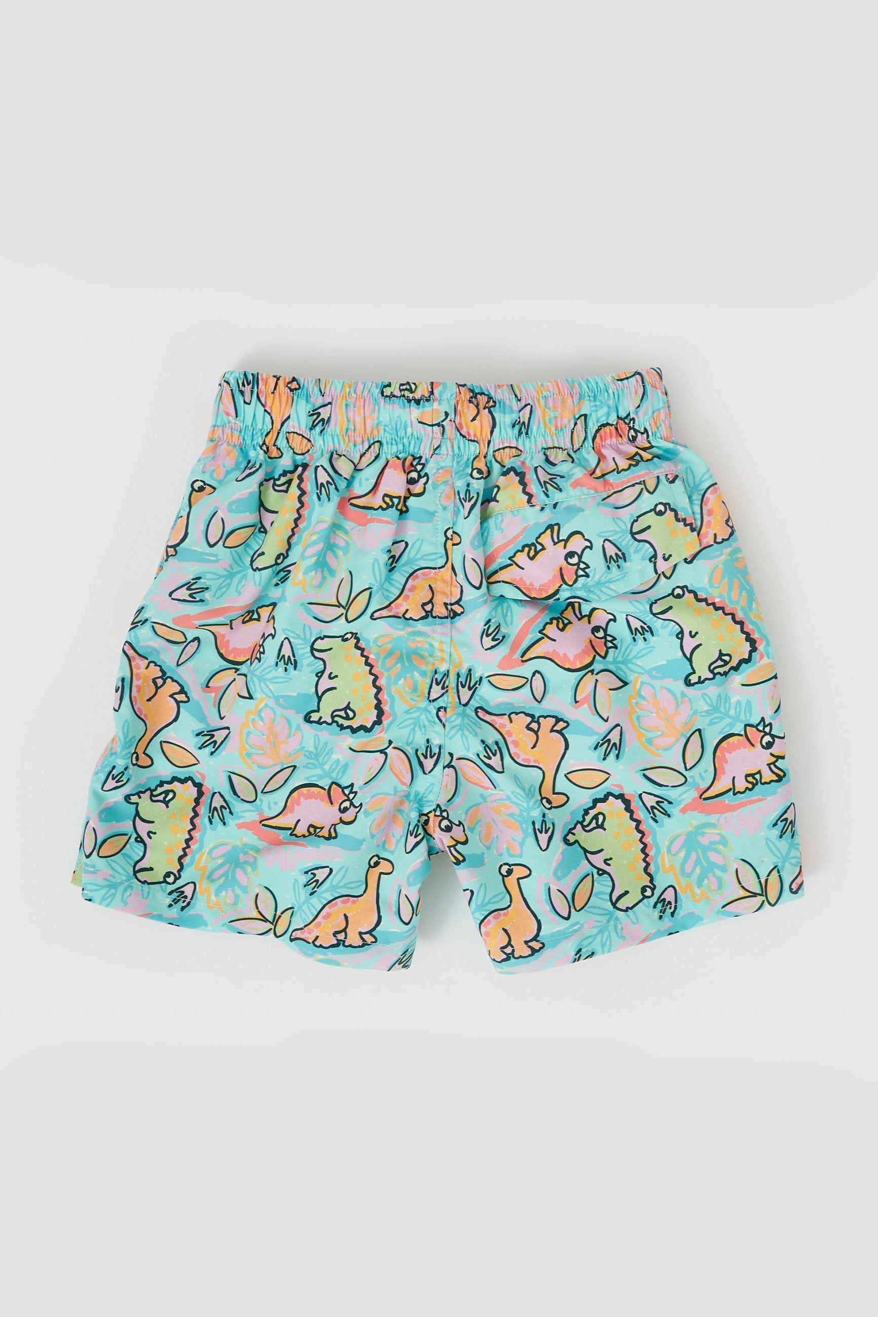 Introducing the Dino Jungle Board Shorts by GOLDIE + ACE: Brightly colored child-sized swim trunks featuring a whimsical dinosaur pattern in orange, green, and yellow. The background is light blue with doodled foliage and water elements. Made from Microfibre Twill and true to size, these shorts have an elastic waistband and a playful, vibrant design.