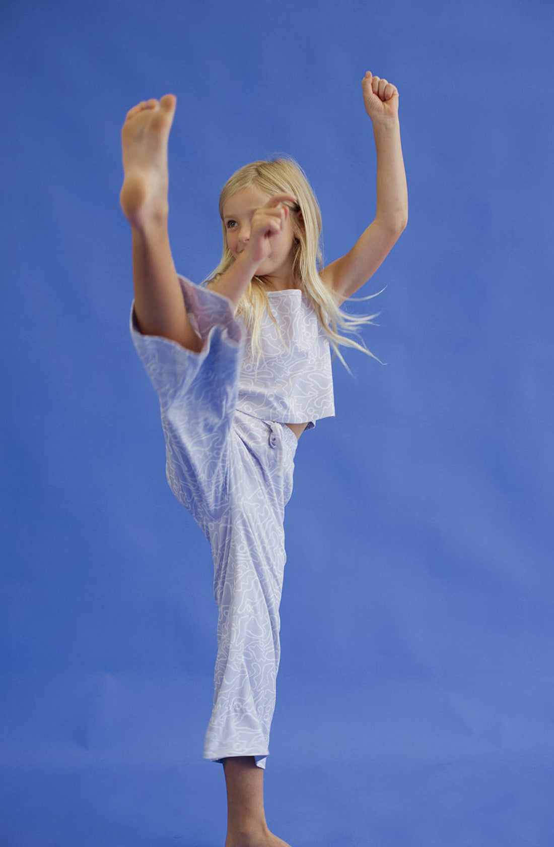 A young girl wearing the forever top and pant in purple with her leg in the air.