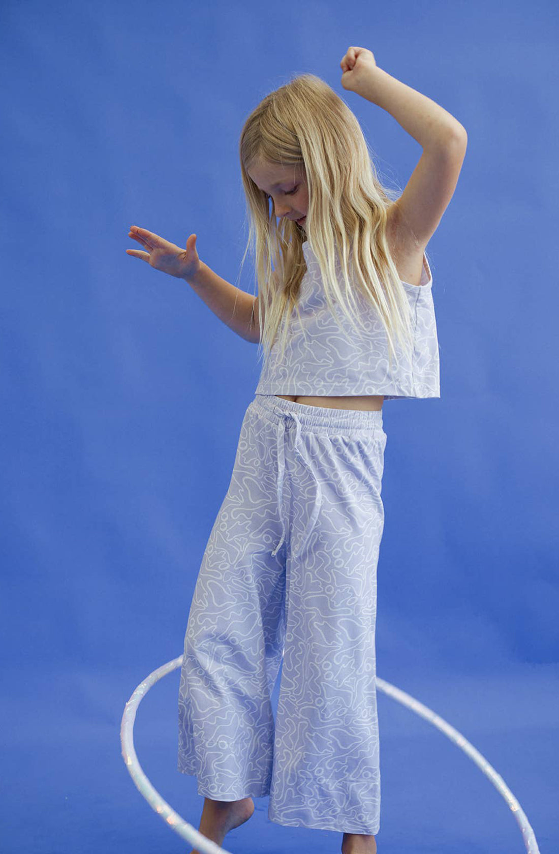 A young girl wearing the forever top and pant in purple spinning a hula hoop around her legs.