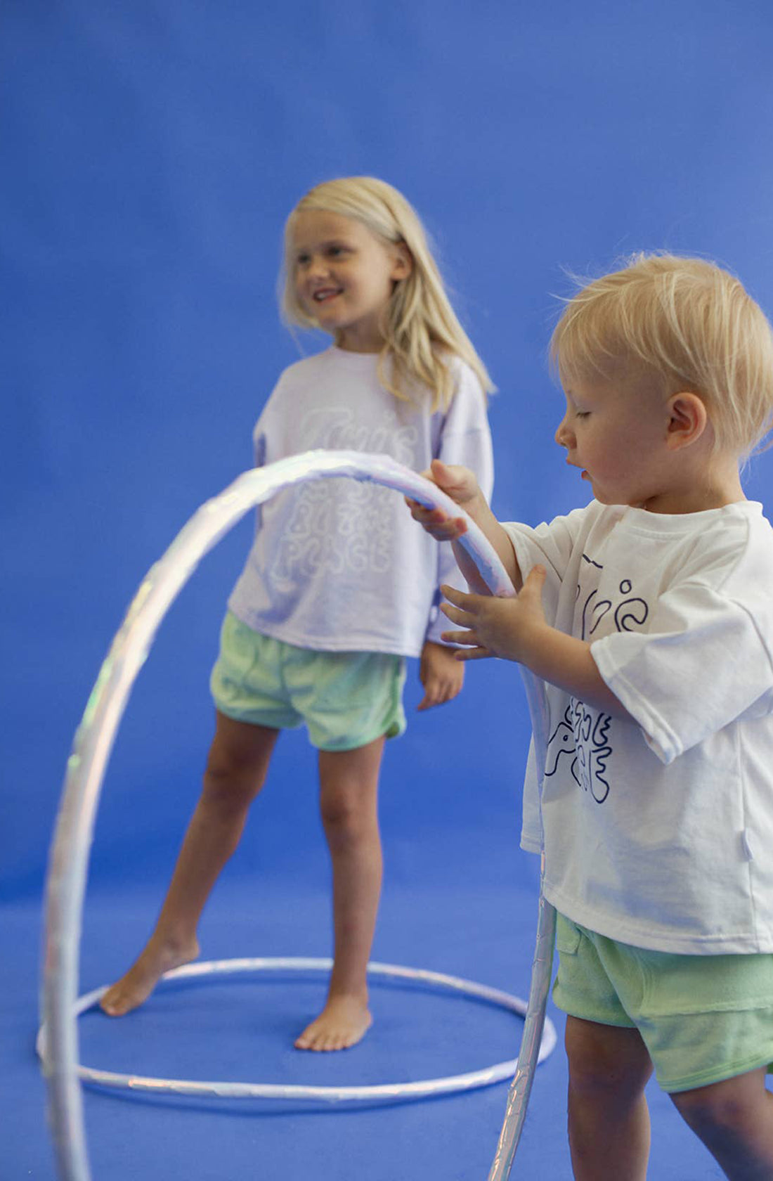 A little boy wearing the homey terry towelling shorts in green holding a hula hoop with a little girl in the background.