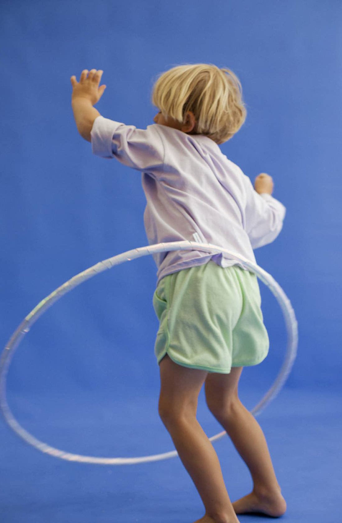 A young boy wearing the homey terry towelling shorts in green spinning a hula hoop around his waist.