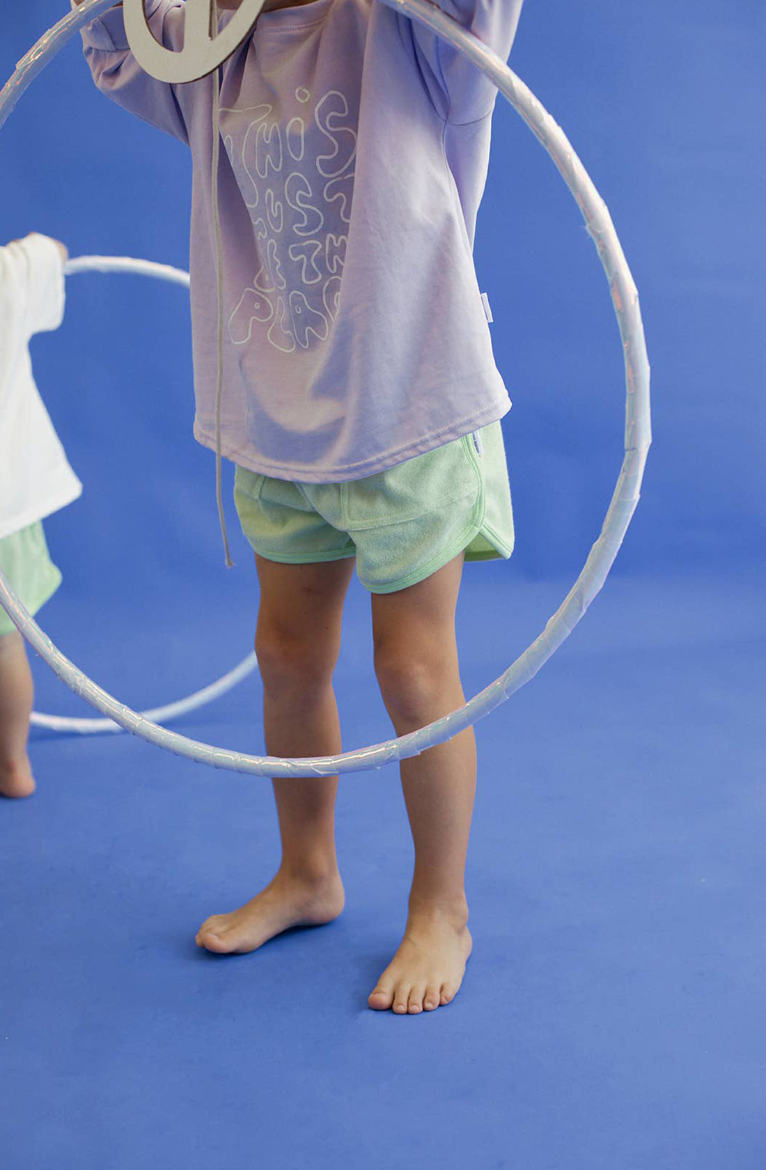 A young boy wearing the homey terry towelling shorts in green while holding a hula hoop.